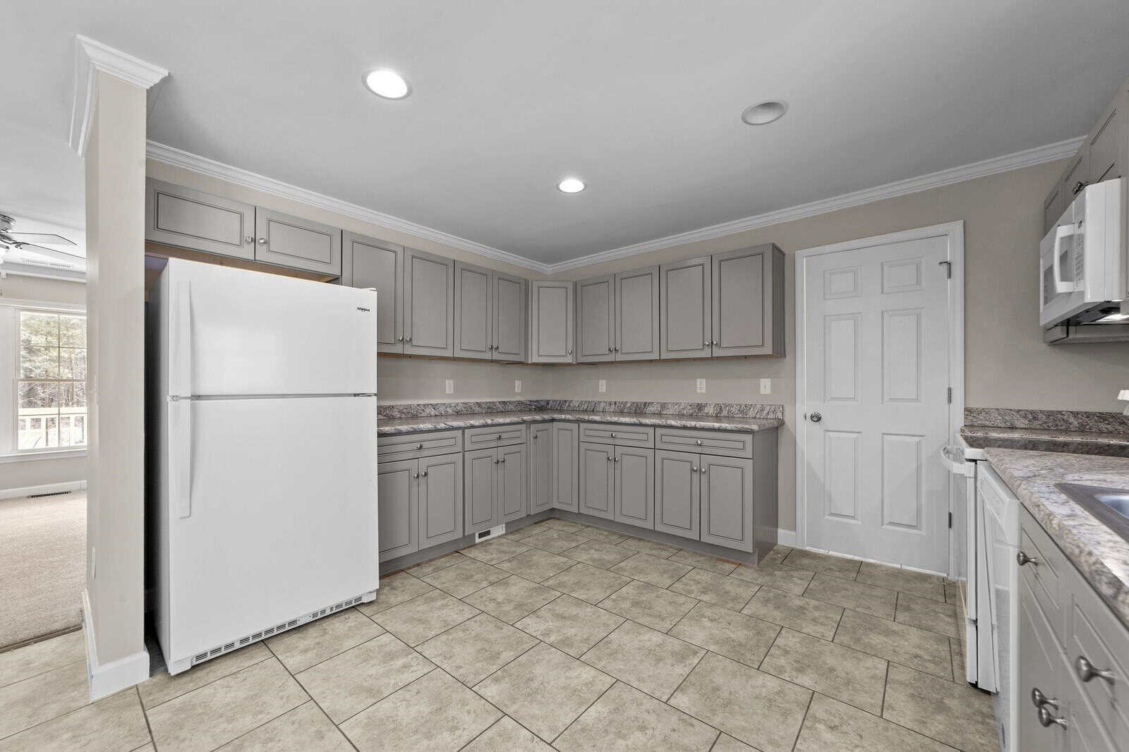A spacious kitchen with gray cabinetry, granite countertops, and modern appliances, featuring ample lighting and tiled flooring.