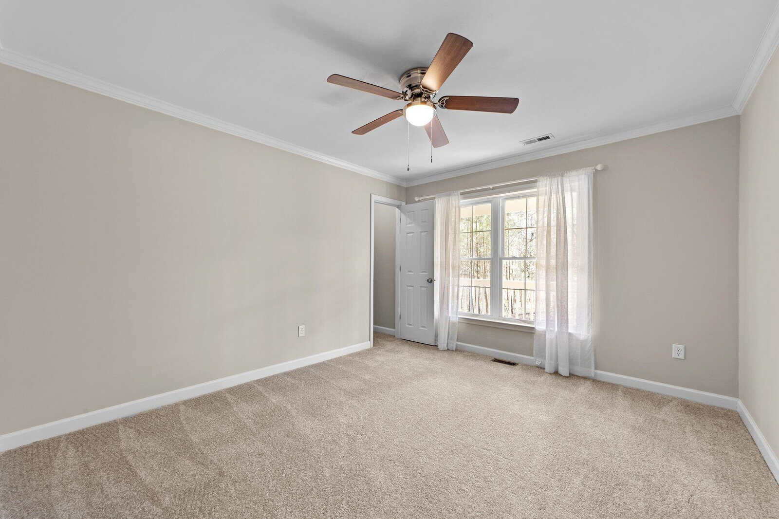 An empty room with beige carpeting, white walls, a ceiling fan, and a glass door leading to a balcony.