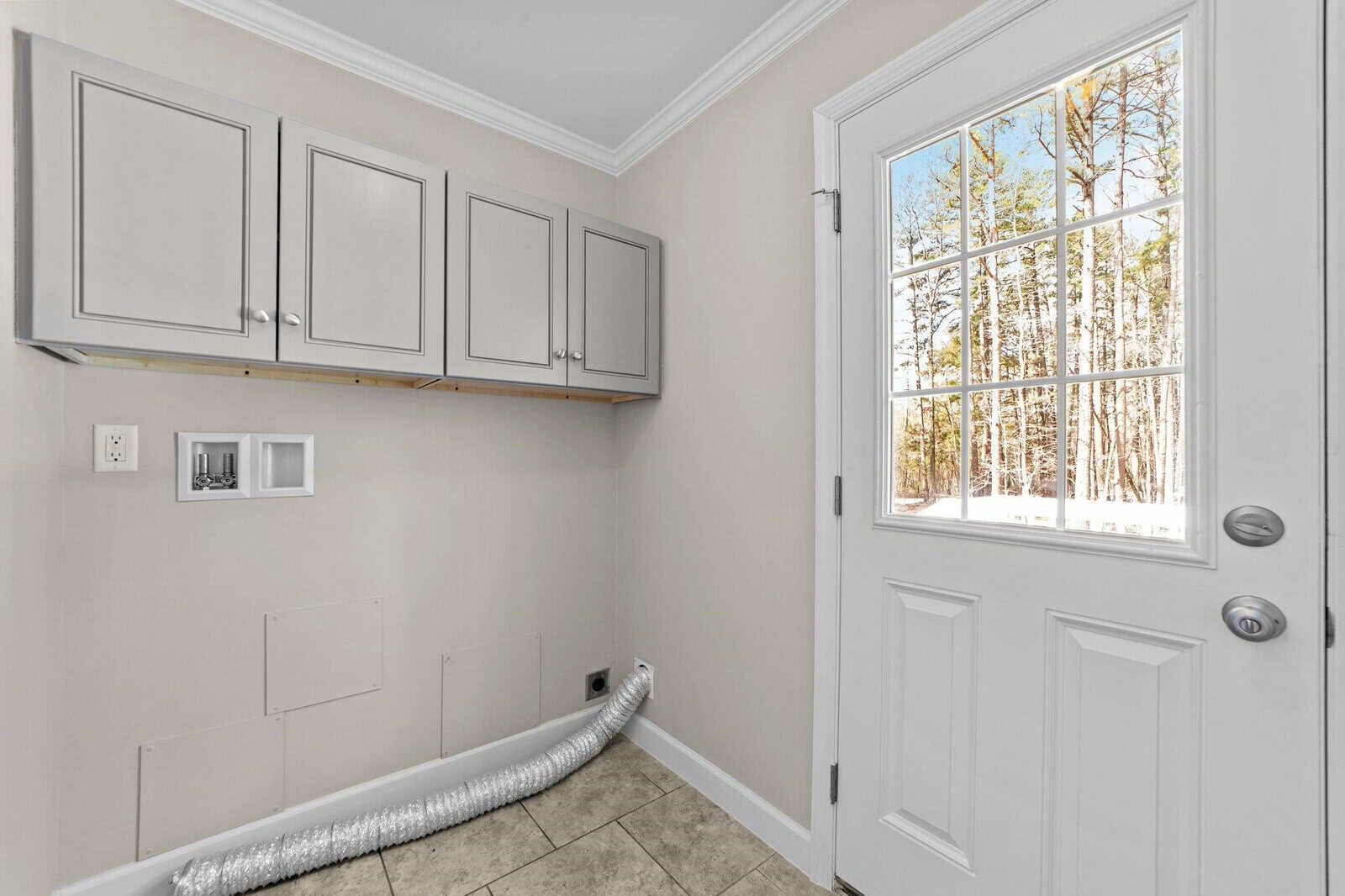 A bright, empty room with tiled flooring and white walls featuring a set of upper cabinets and a glass-paned door that looks out onto a wooded area with snow on the ground.