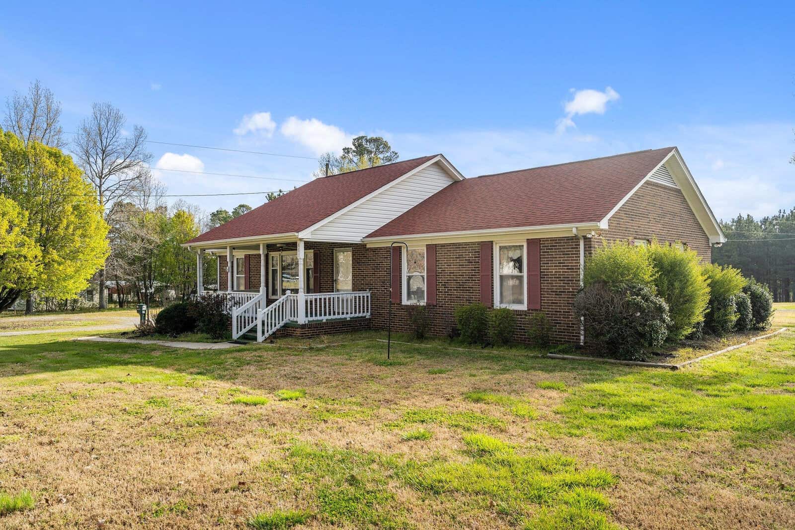 Single-story brick house with a gabled roof and a small front porch, set on a grassy lawn with a clear sky above.