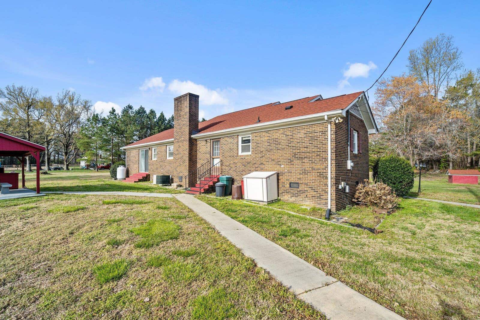 A single-story brick house with a prominent chimney and a well-kept lawn on a sunny day.