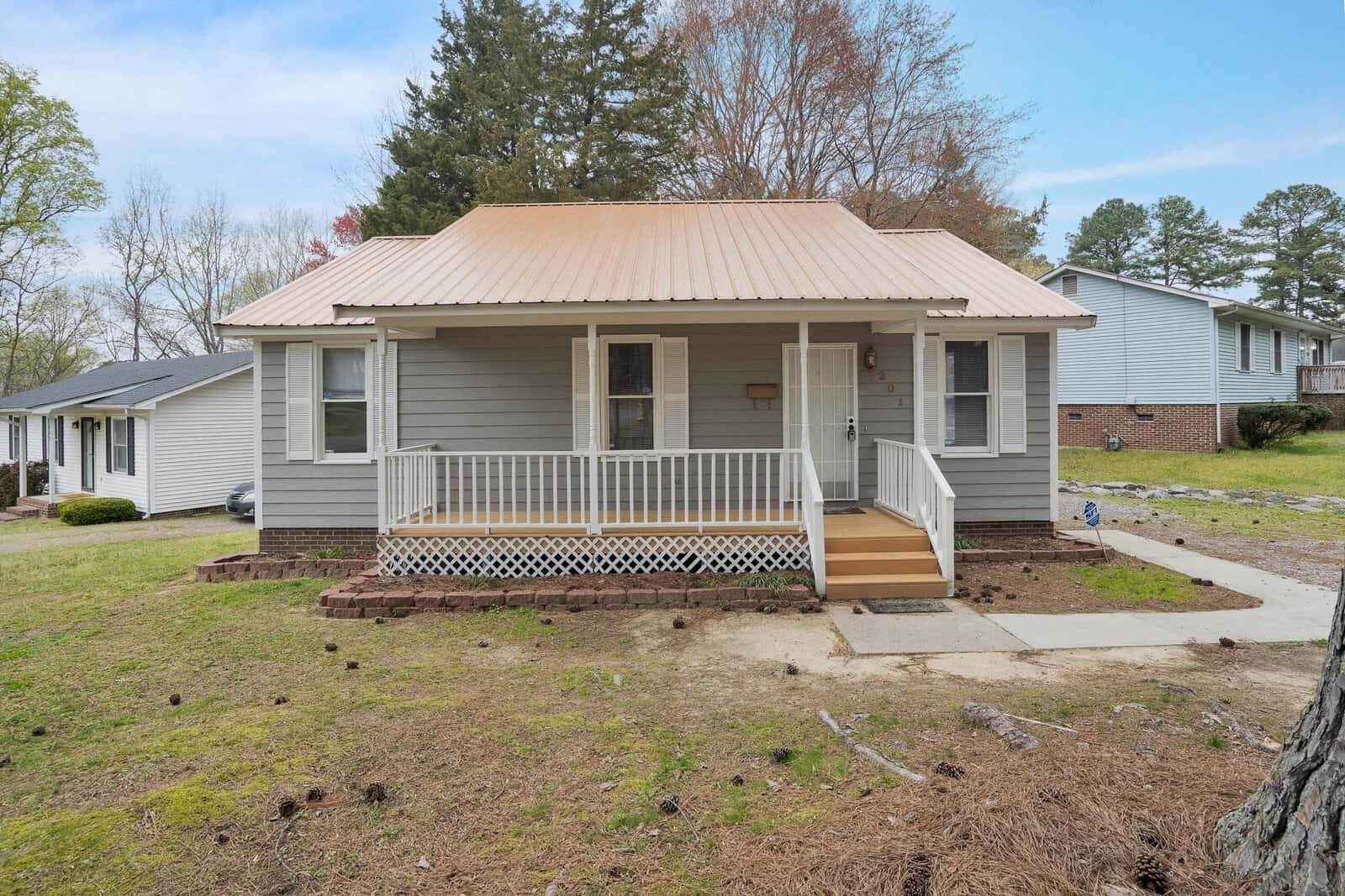 A single-story house at 201 Ranes Drive, Henderson NC, with a tan roof and a front porch, set against a residential backdrop with a front lawn showing patches of dirt and a bare tree
