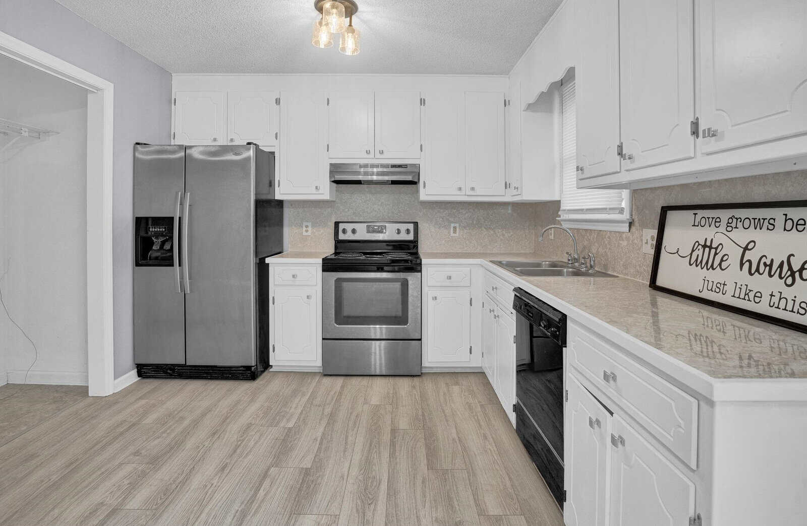 A modern kitchen with white cabinetry, stainless steel appliances, and a decorative sign on the counter.