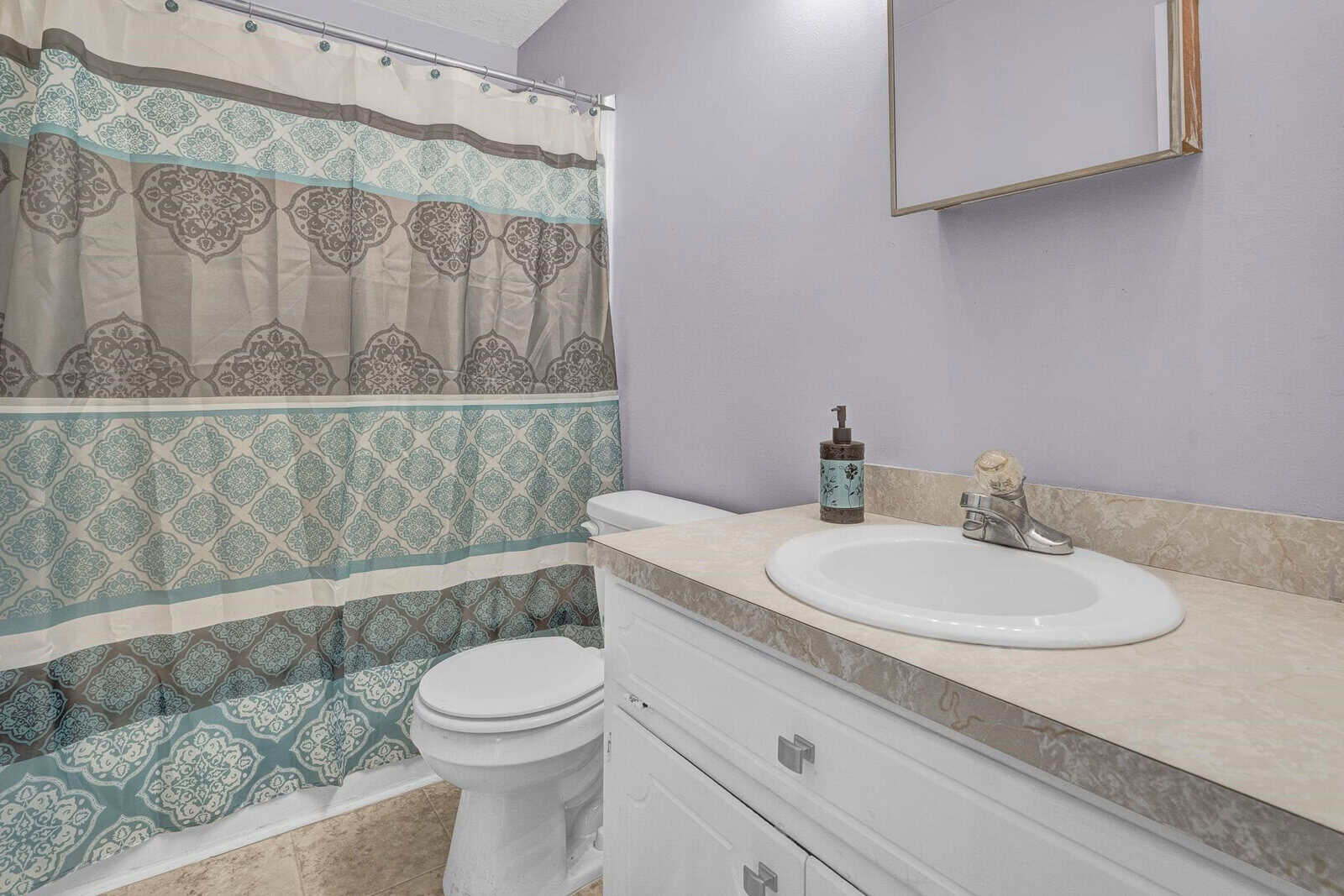 A clean and tidy bathroom featuring a patterned shower curtain, white toilet, and a vanity with a sink. there are a few toiletry items on the countertop.