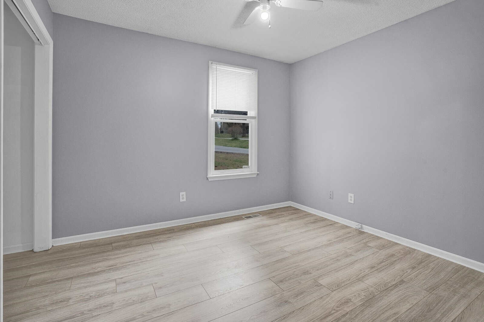 Empty room with light purple walls, a single window, and laminate flooring.