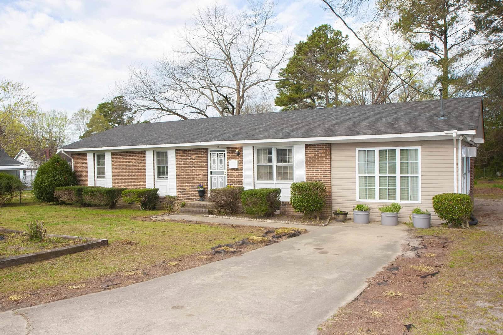 Single-story brick residential house with large front windows and a concrete driveway, located at 425 Norvell Street, Henderson NC, set against a background of trees and a clear sky.