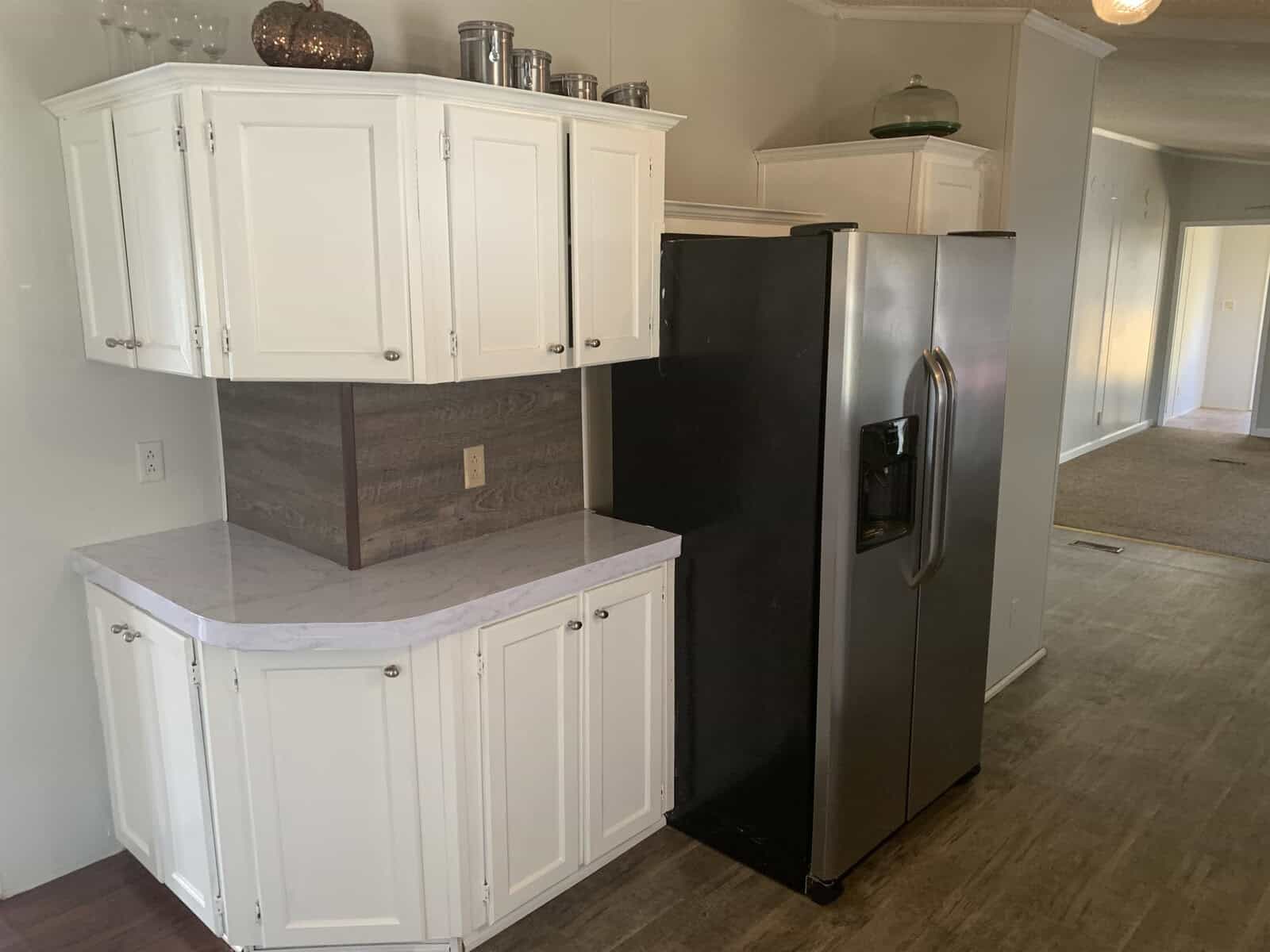 A kitchen corner with white cabinetry and a black refrigerator next to a countertop with a wood-patterned backsplash.
