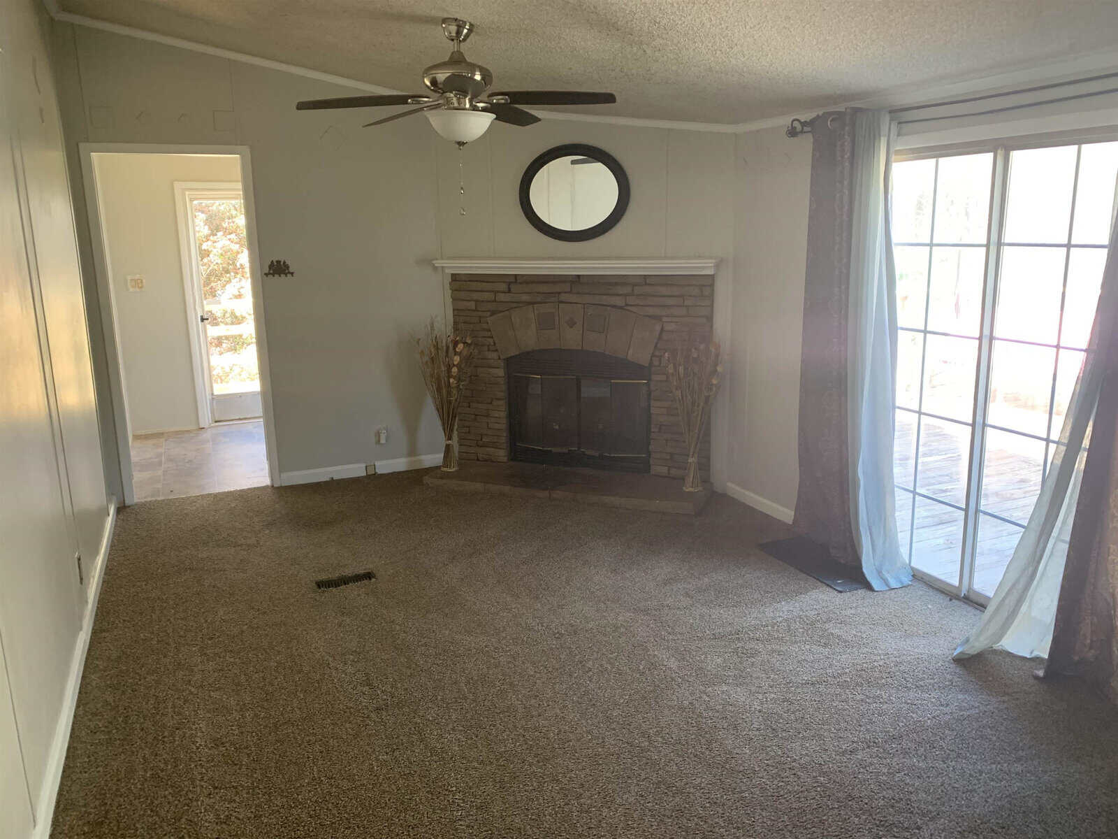 A living room with carpet flooring featuring a fireplace, ceiling fan, and sliding glass door with daylight streaming in.