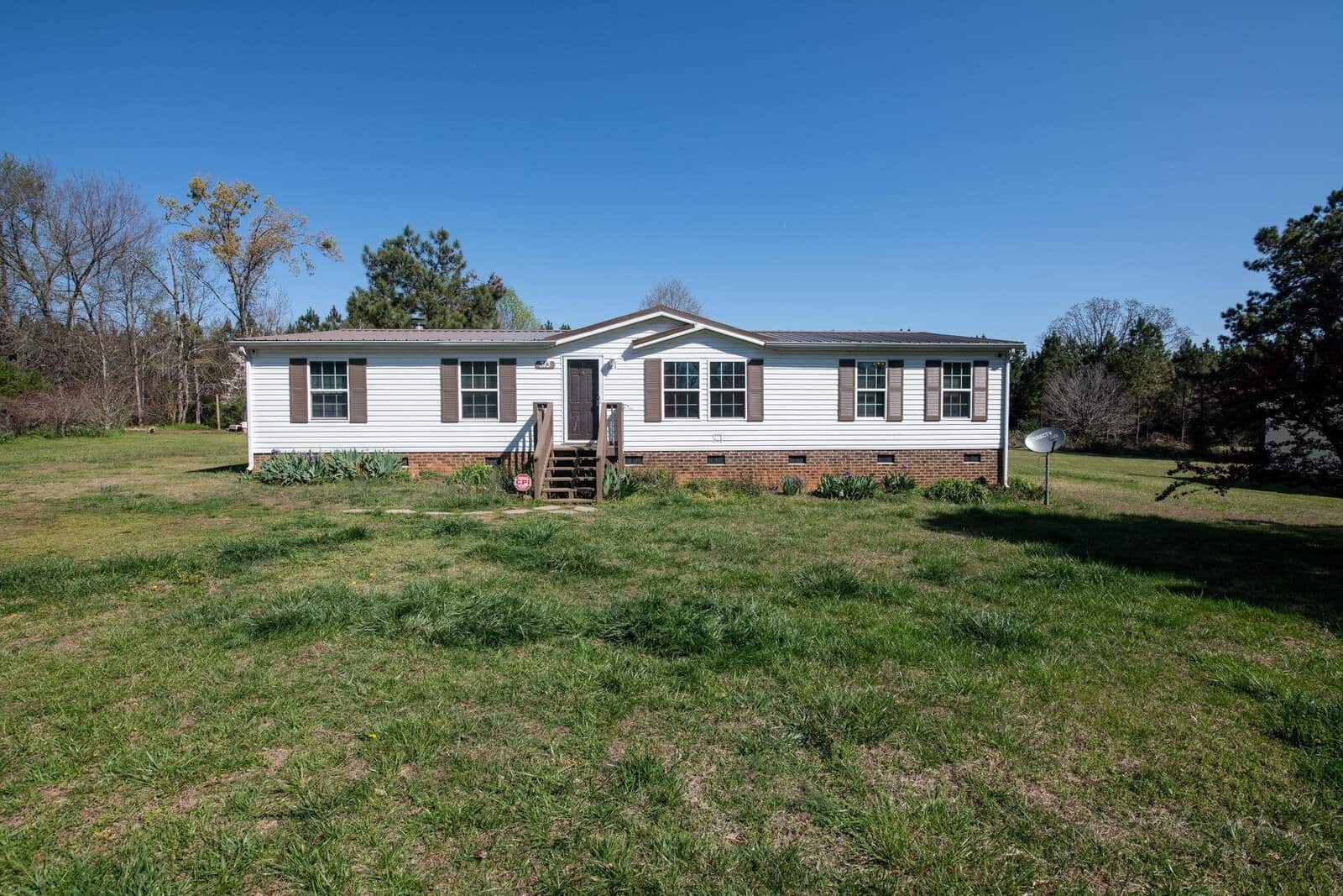 A single-story residential mobile home at 313 Plum Nutty Road, Henderson NC, with vinyl siding, steps leading to the front door, and a satellite dish in the yard, set against a clear