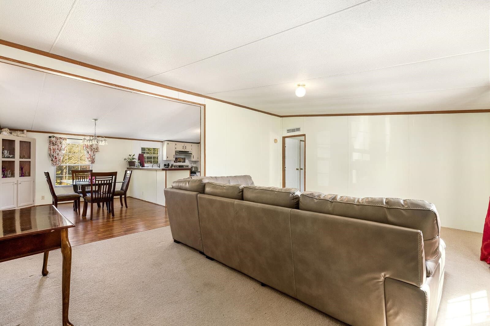 A spacious living room featuring a large brown leather sectional sofa, with an adjoining dining area in the background and a door leading out of the room.