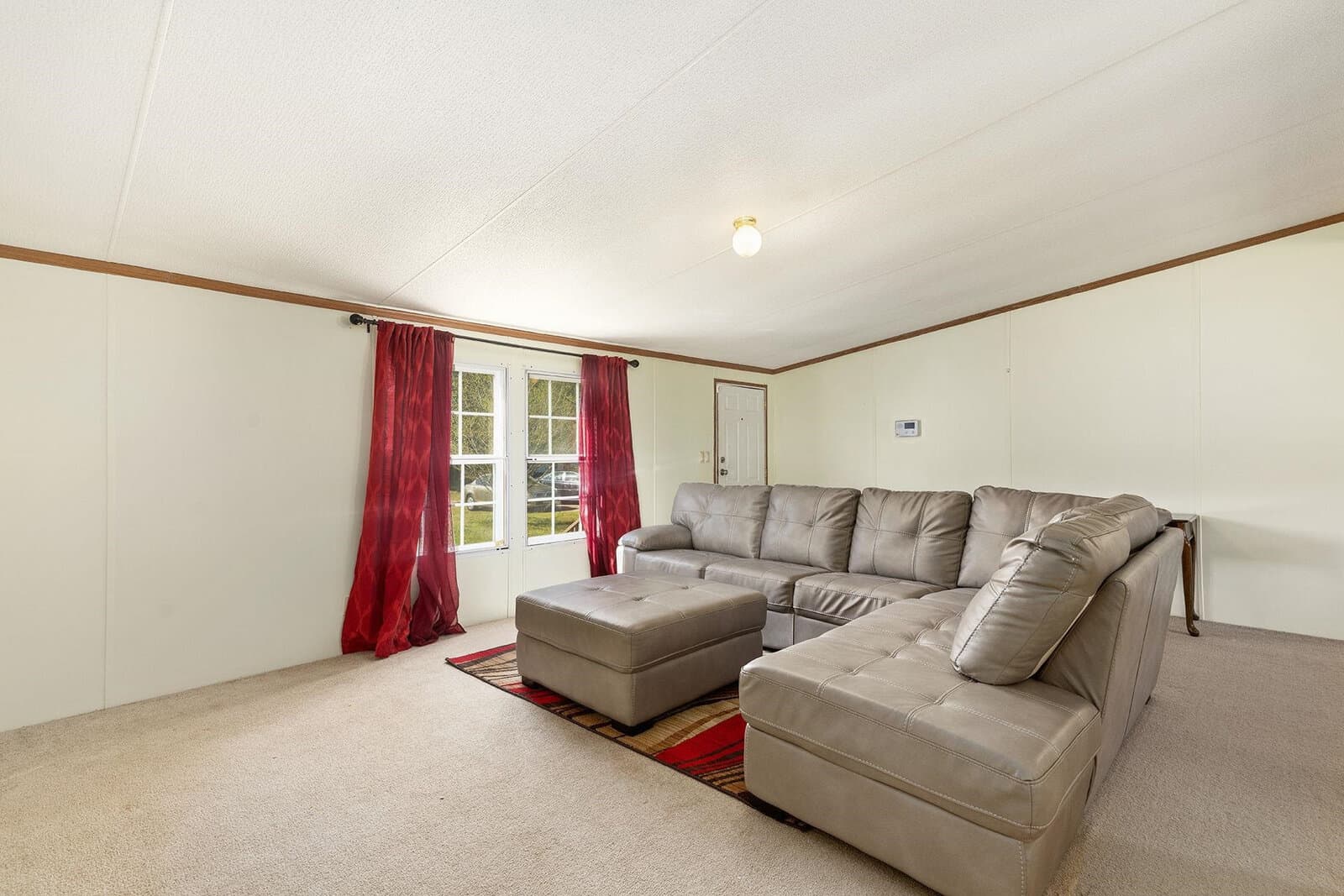 Spacious living room with a gray sectional sofa, matching ottoman, red curtains, and a glass door leading outside.