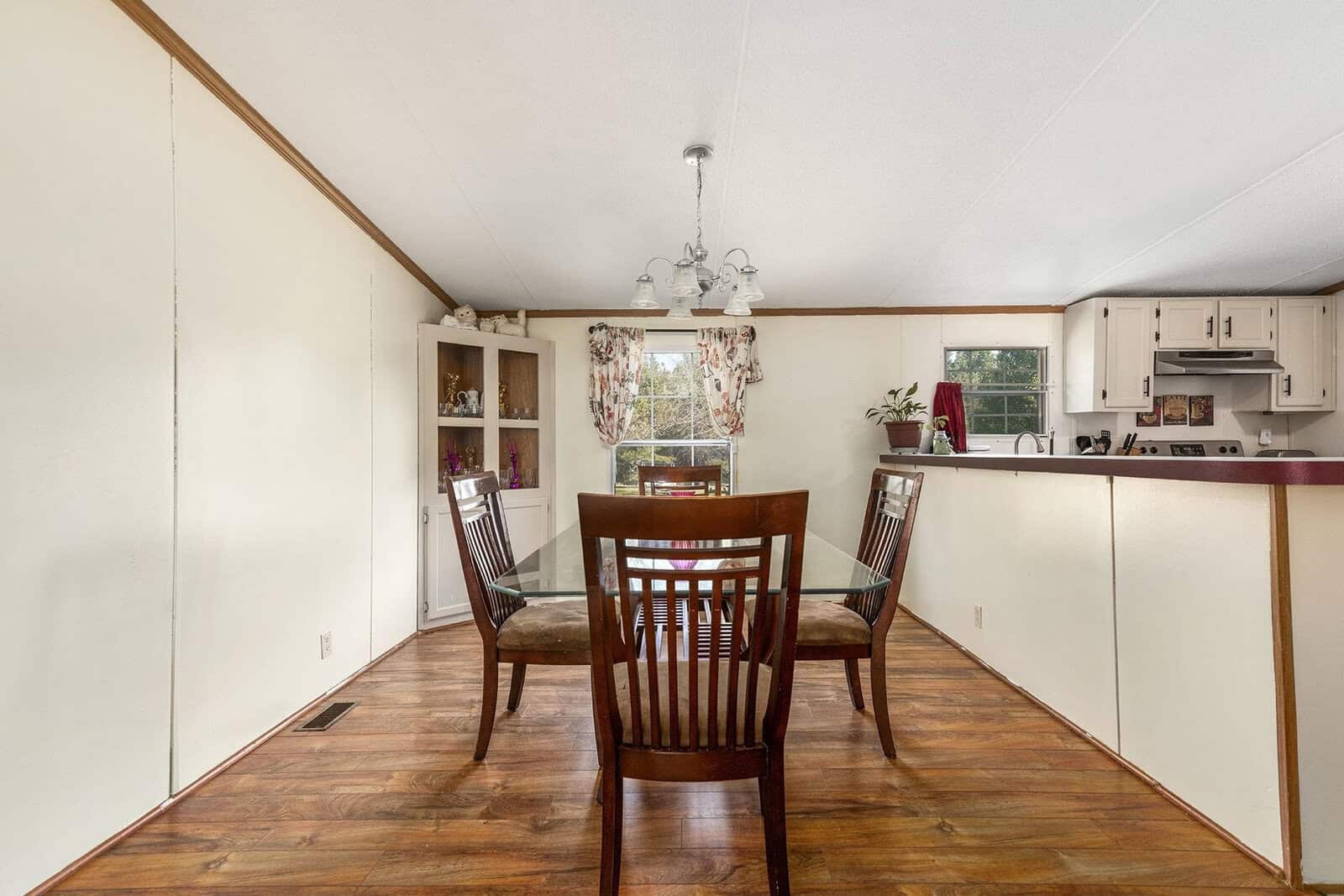 A modest dining area with a wooden table and chairs, adjacent to a kitchen with white cabinets and laminate flooring.