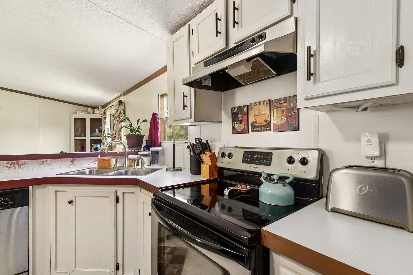 A compact kitchen with white cabinets, black countertops, and white appliances, including a stove and a toaster on the counter. a blue kettle sits on the stove.