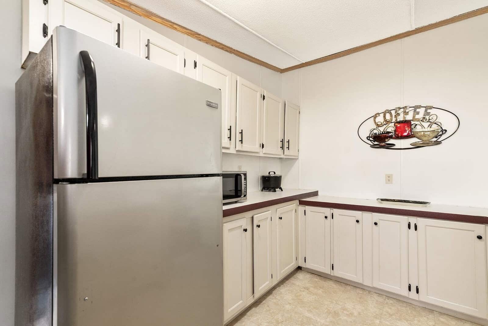 A tidy kitchen with white cabinetry, a stainless steel refrigerator, and a coffee-themed wall decoration.