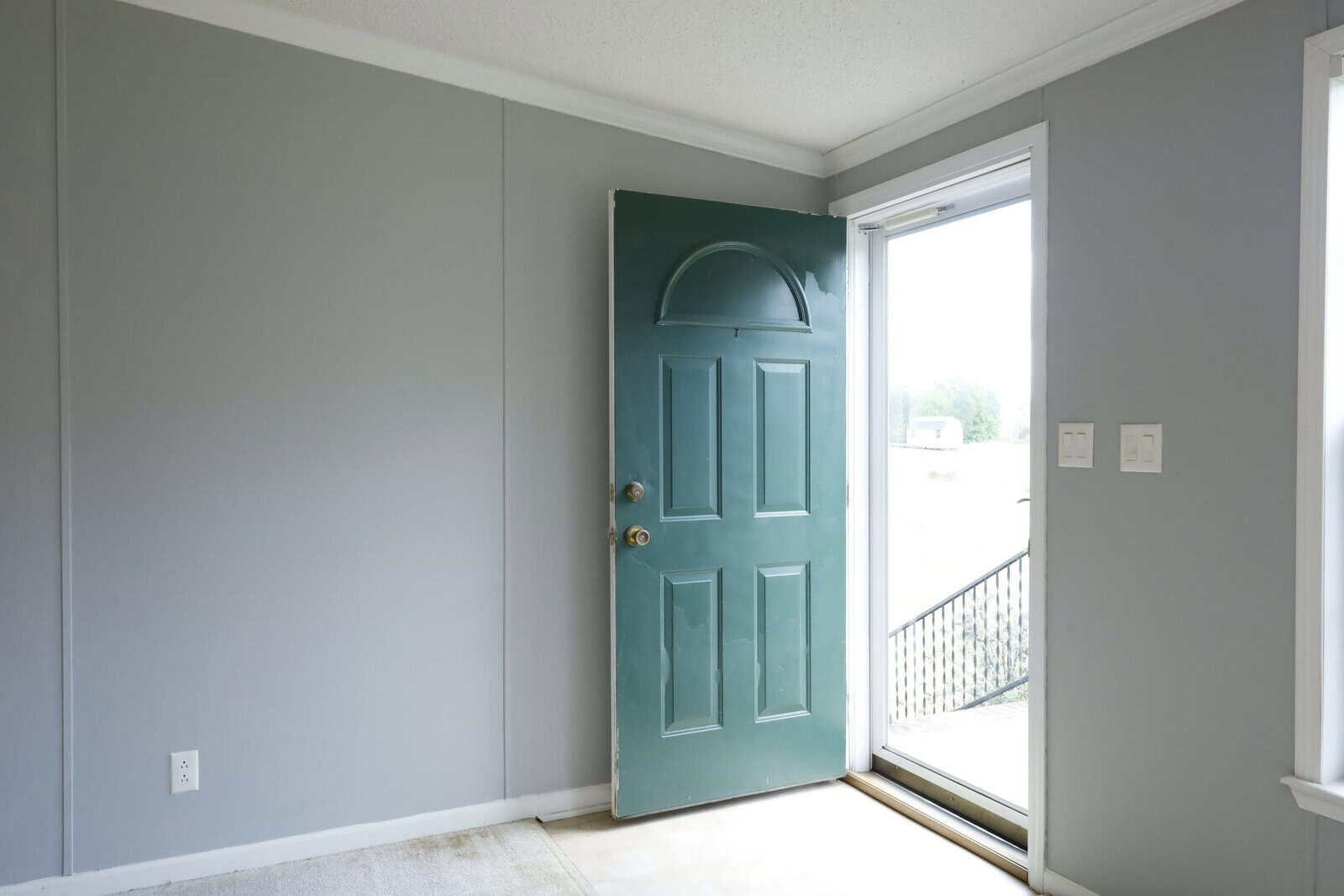 An open teal door leading to a balcony in a room with gray walls and white trim.