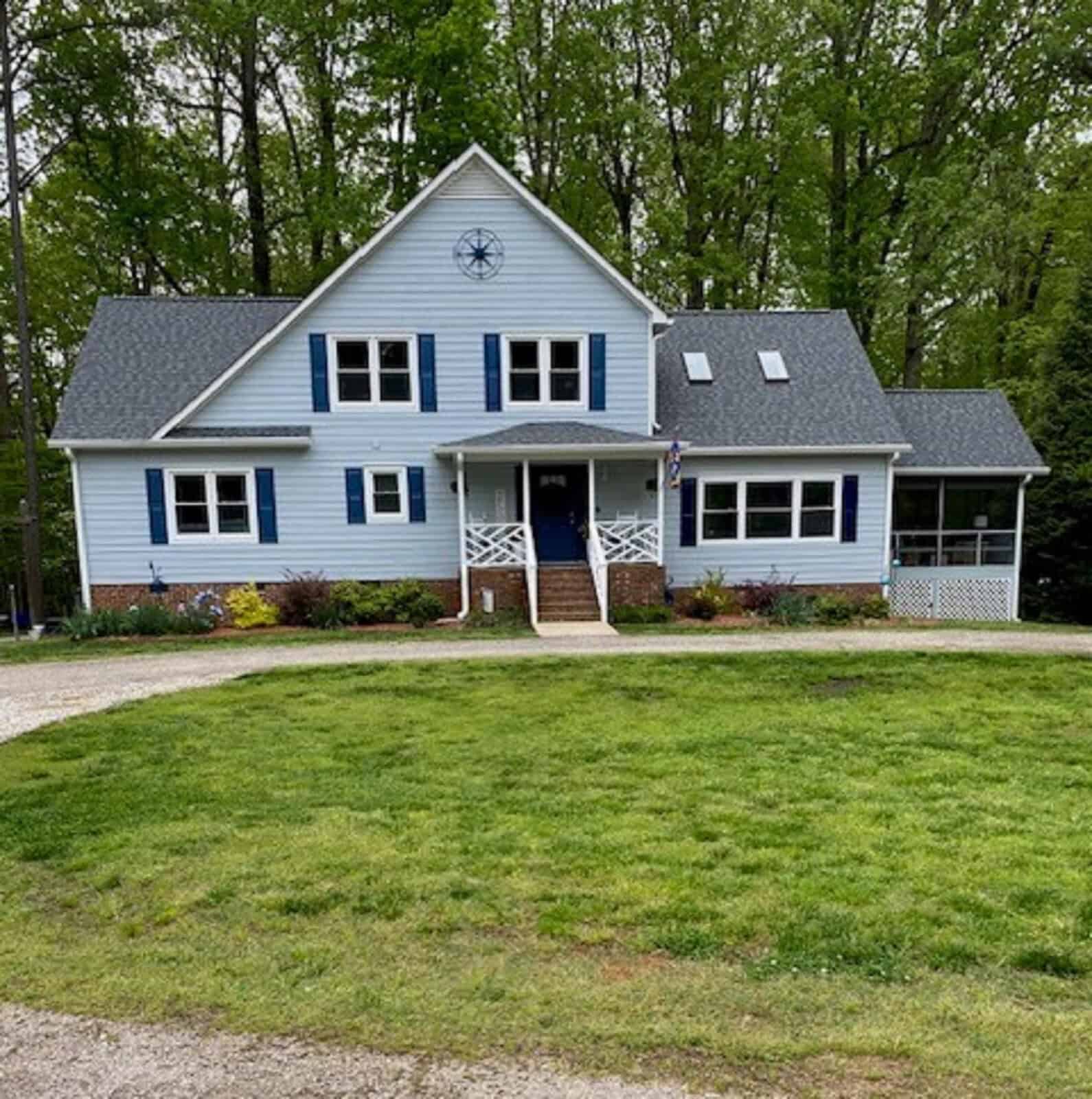 A two-story blue house with white trim, a front door flanked by two windows, and an attached screened porch at 87 Edgewater Lane, set against a backdrop of trees.