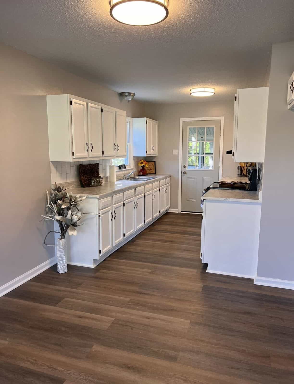 A spacious kitchen with white cabinetry, stainless steel appliances, and wooden flooring, featuring a door with glass panels.