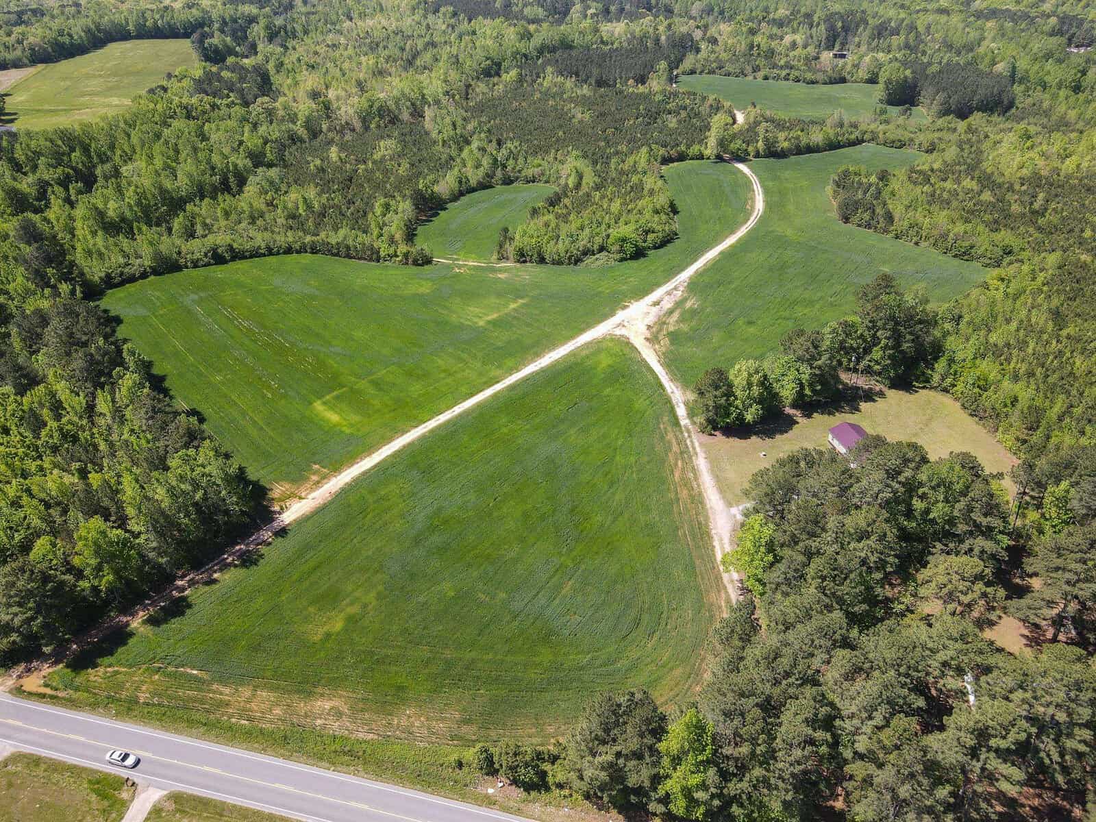 Aerial view of a large green field intersected by pathways and surrounded by trees, with Vicksboro Road along the bottom edge of the frame in Henderson, NC.