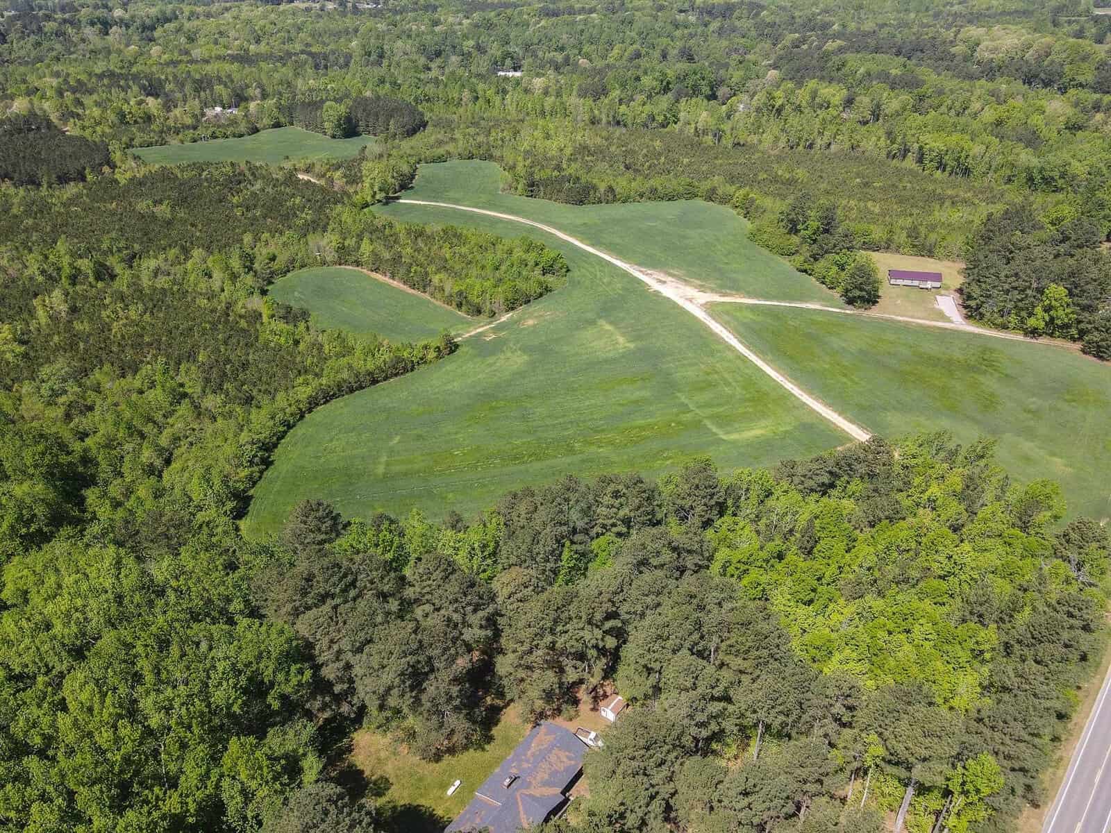 Aerial view of a green landscape with patches of forest, a road cutting through the scene, and a building at the bottom edge.