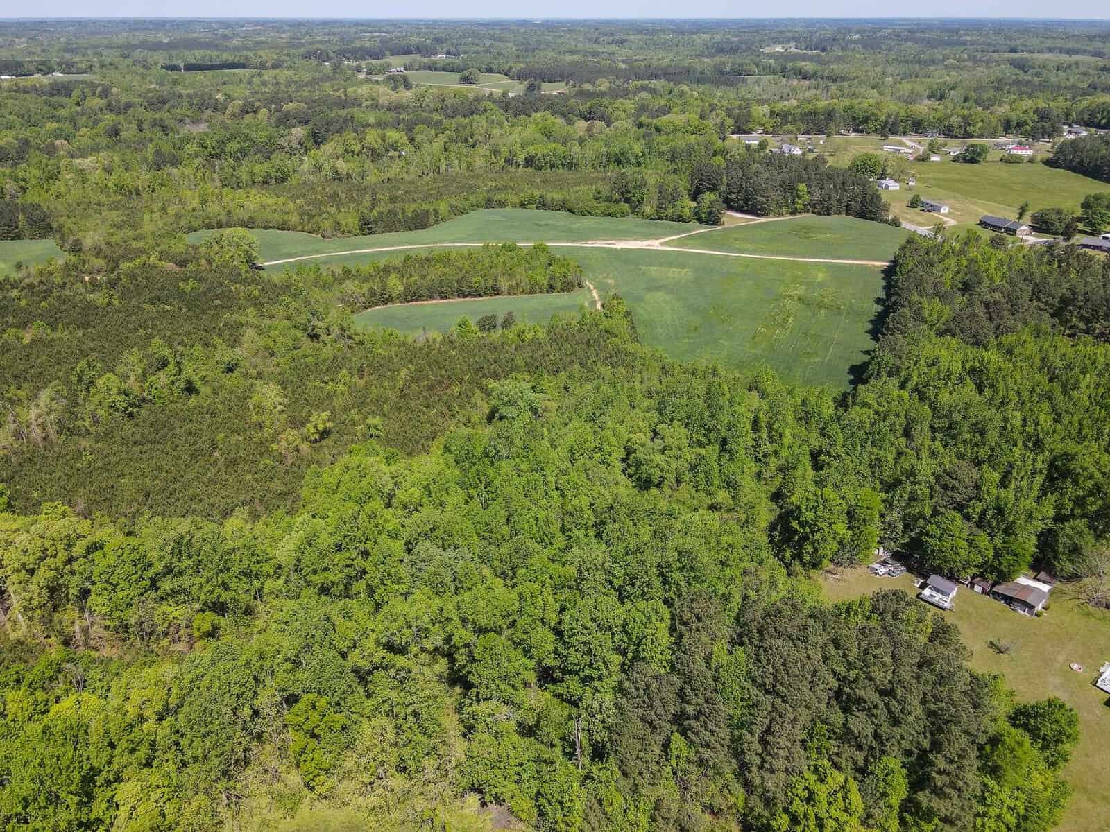 An aerial view showing a patchwork of fields, forests, and a pond in a rural landscape.