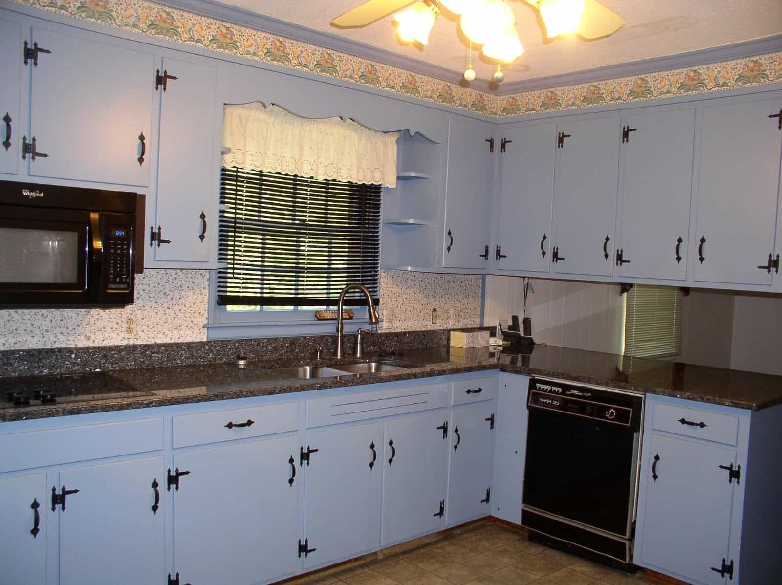 A well-lit kitchen featuring blue cabinetry, granite countertops, and a mix of black and white appliances.