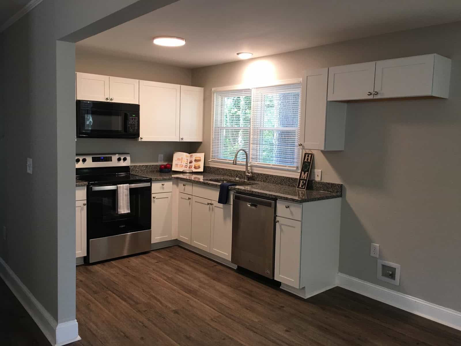 A modern kitchen with stainless steel appliances, white cabinetry, and wood-look flooring.