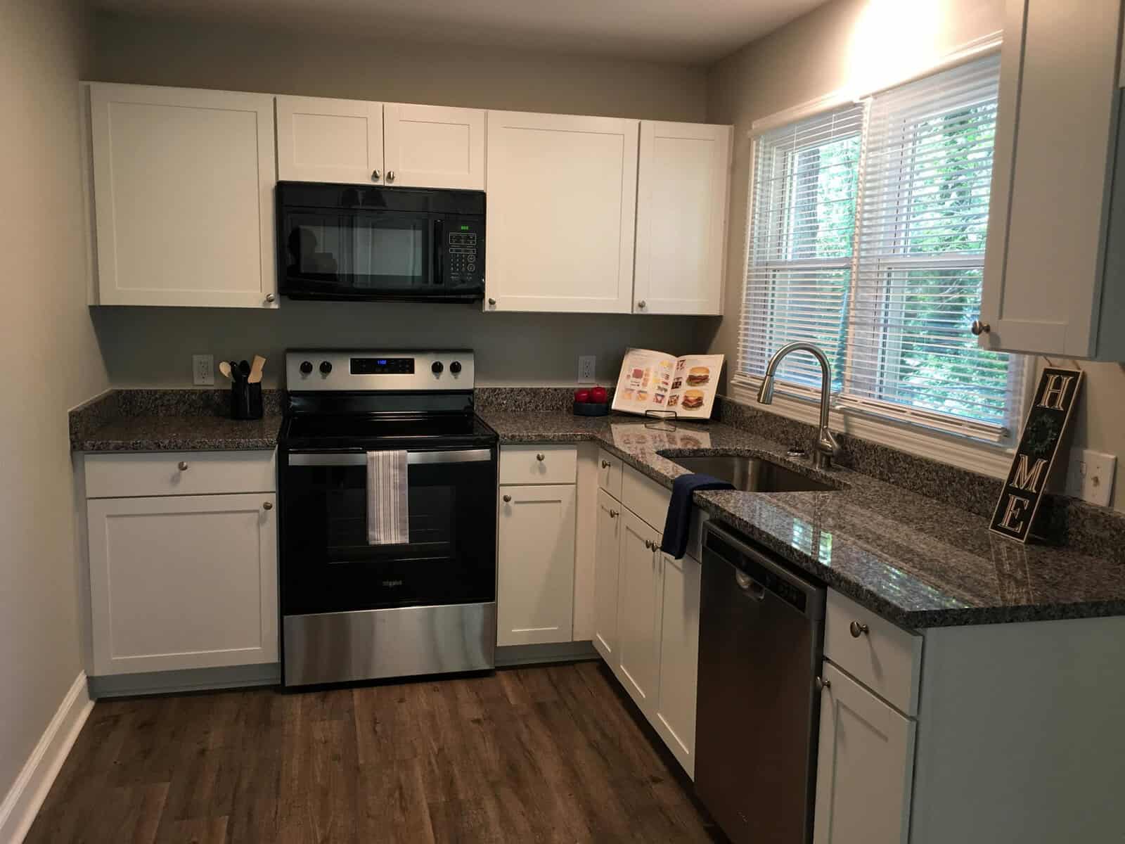 A modern kitchen interior with white cabinetry, granite countertops, stainless steel appliances, and a window above the sink.