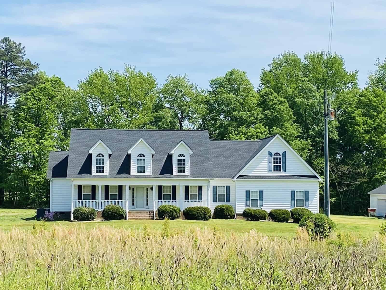 A white single-story house with a gabled roof and four dormer windows situates amid a grassy field under a clear sky at 324 Kelly Road, Henderson NC.