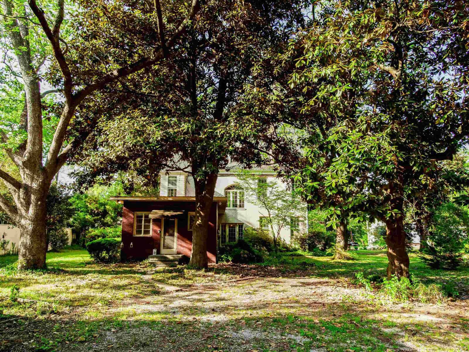 A two-story house partially shaded by large trees on a sunny day.
