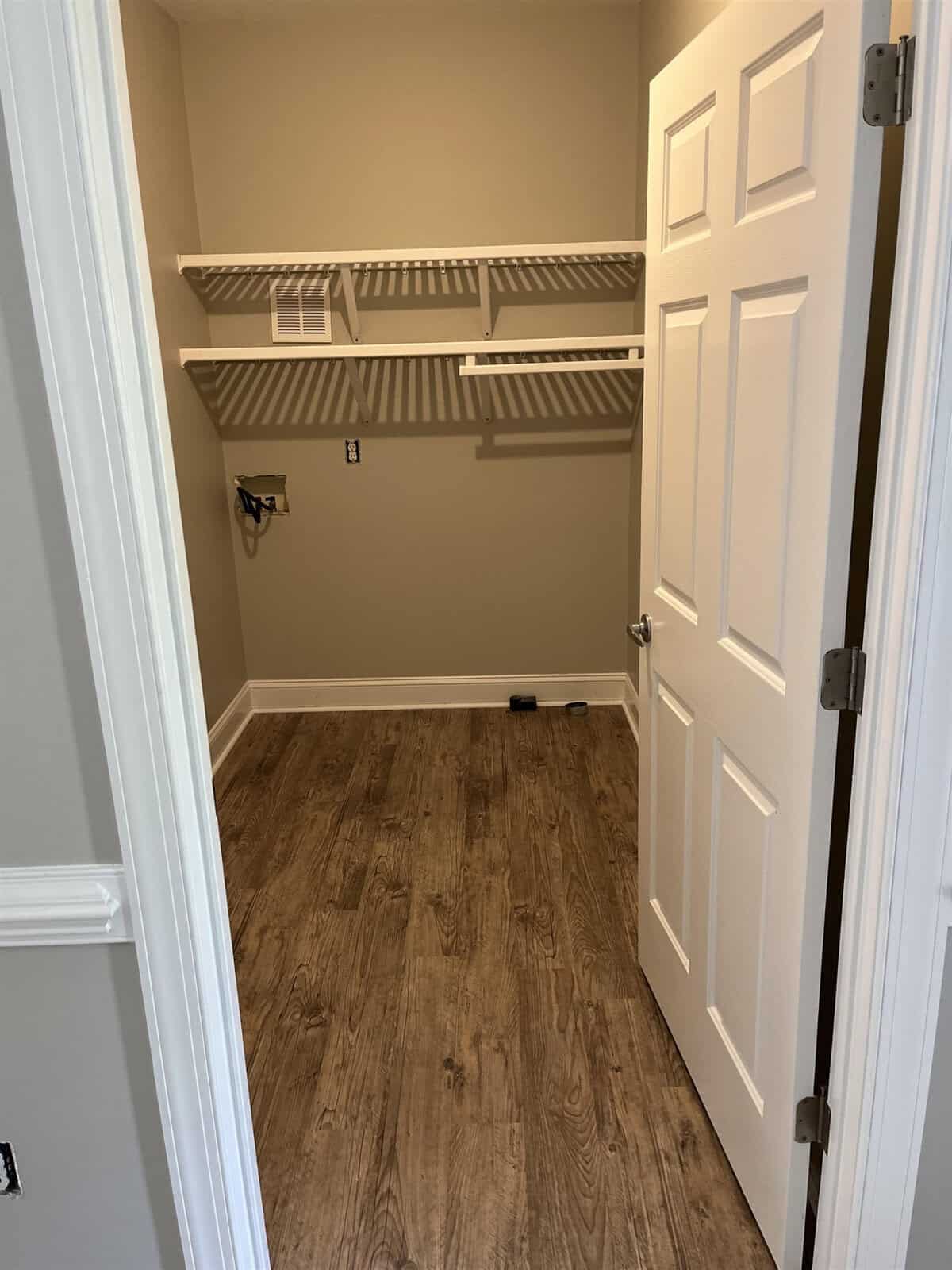 An empty closet with built-in shelves and a wooden floor, viewed from the doorway.