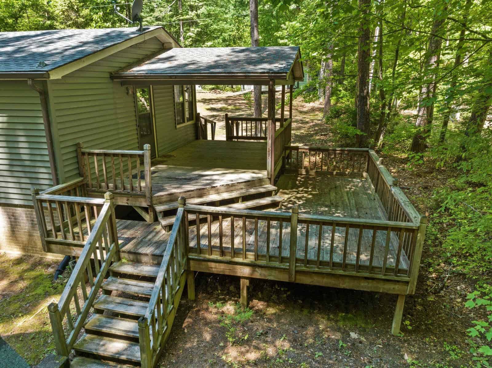 A wooden deck with stairs leads to the entrance of a house surrounded by lush green trees.