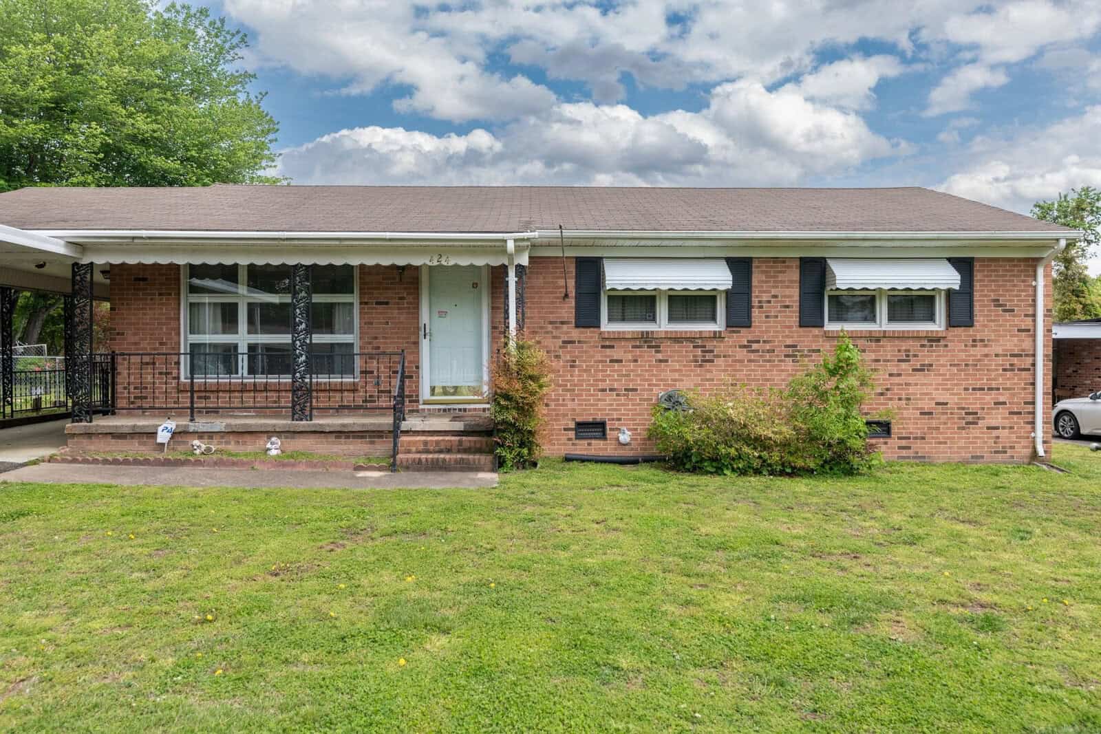 Single-story brick suburban house with a covered front porch and white door, under a partly cloudy sky.