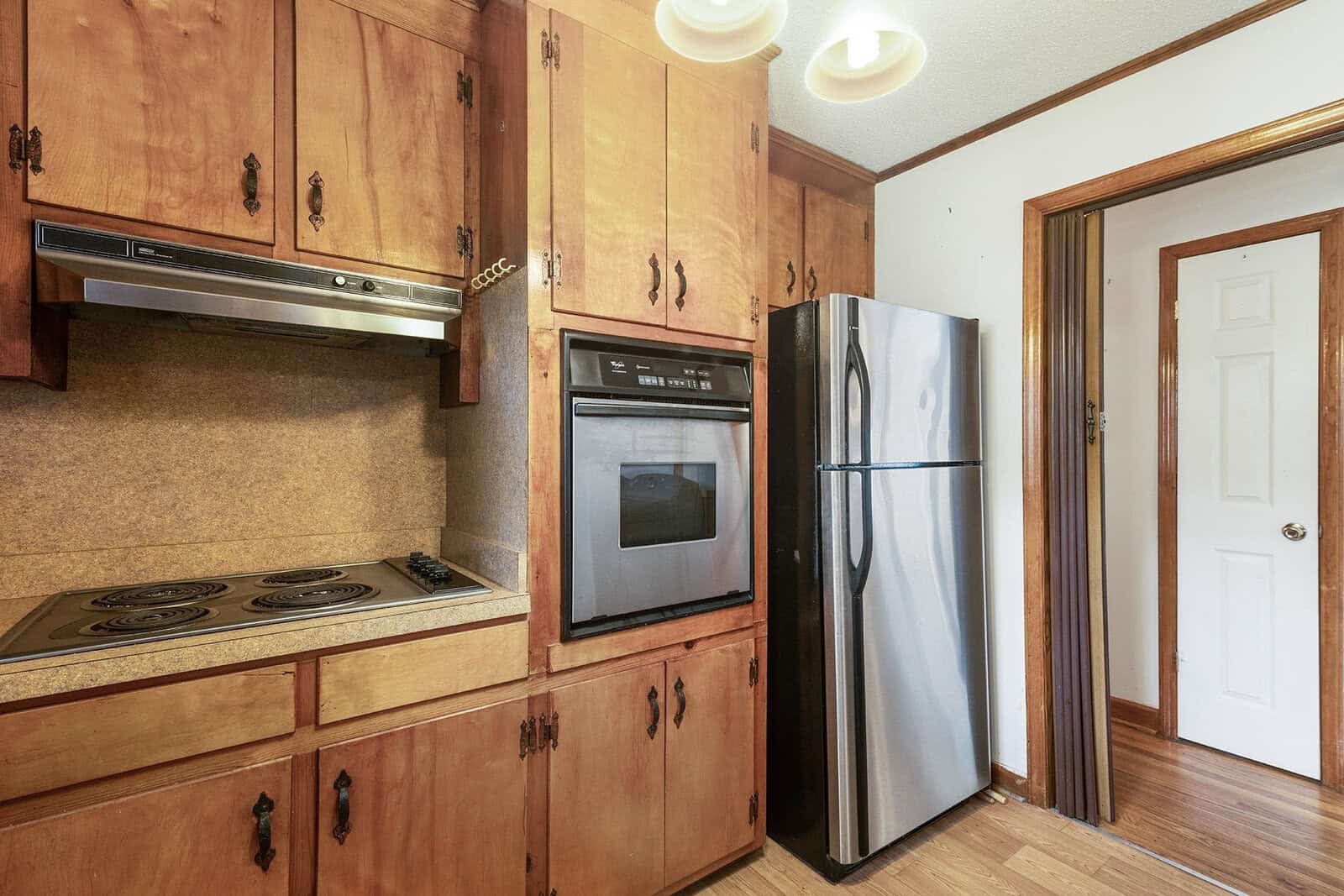 A kitchen interior featuring wooden cabinets, a built-in oven, stovetop, and a side-by-side refrigerator next to a door.