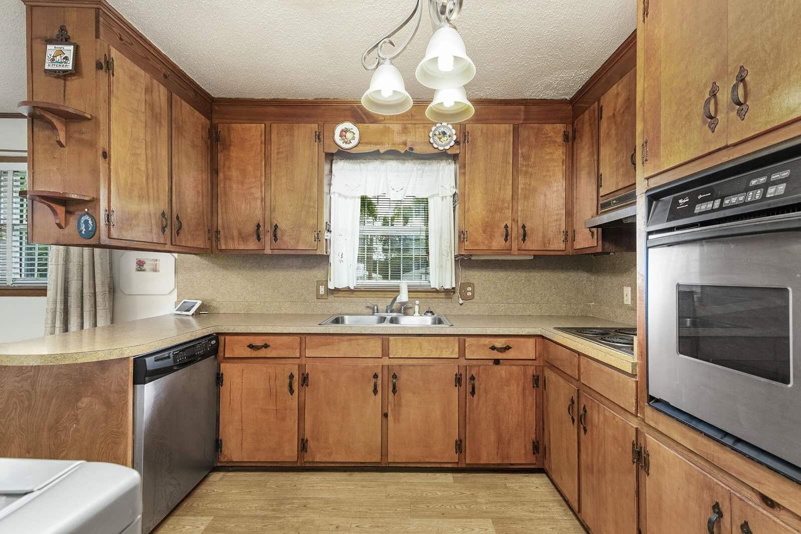A well-lit kitchen interior with wooden cabinets, laminate countertops, a double basin sink, and white appliances.