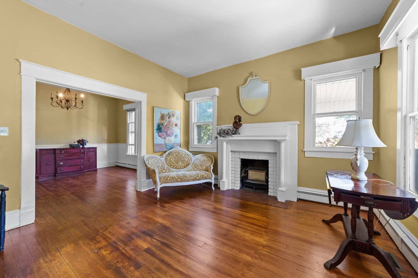 Elegant living space with glossy hardwood floors, a white fireplace, traditional furniture, and a splash of color from a modern painting on the wall.
