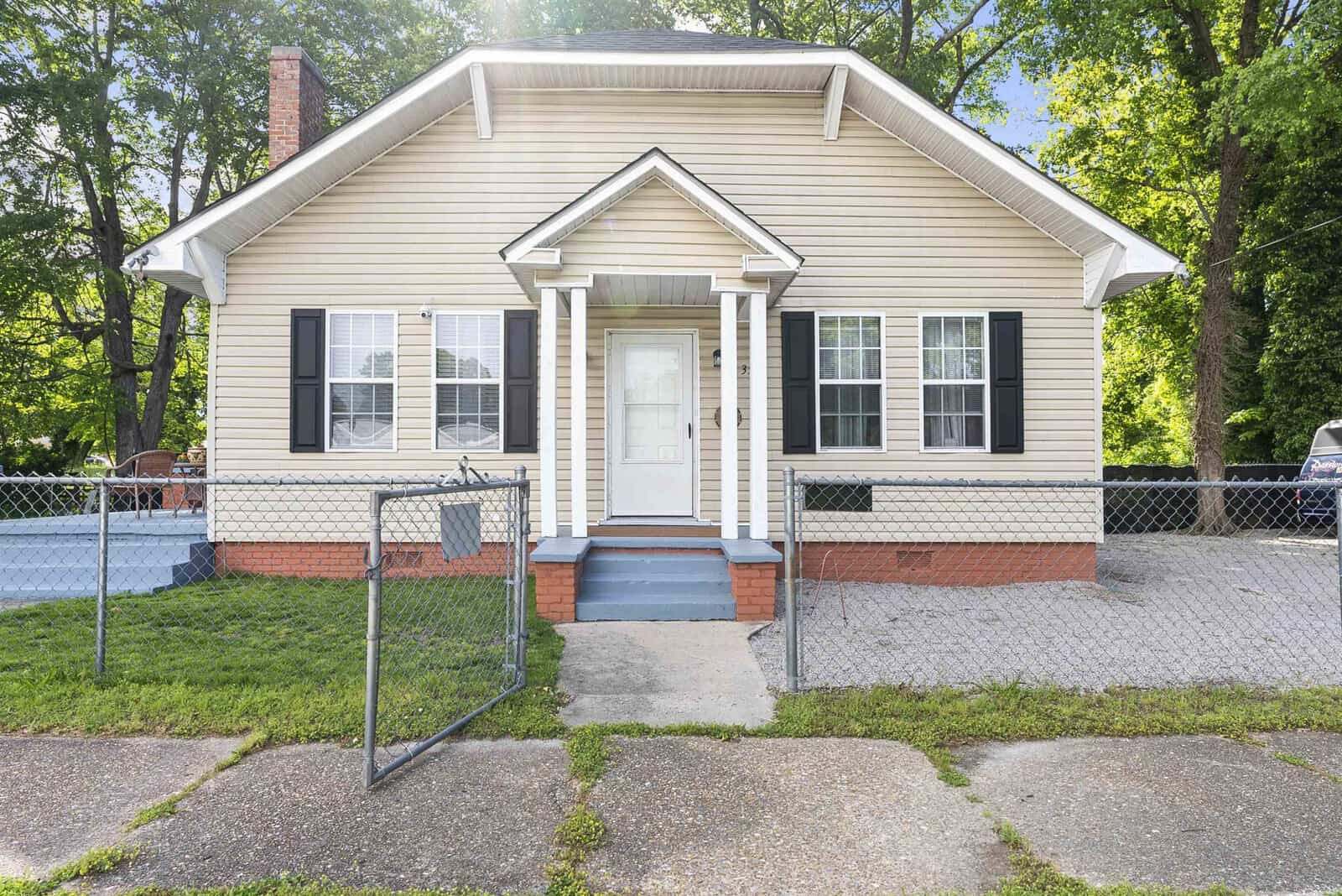 A single-story tan house at 350 N Clark Street, Henderson NC, with white trim and a small front porch, enclosed by a low chain-link fence, with a concrete walkway leading to the