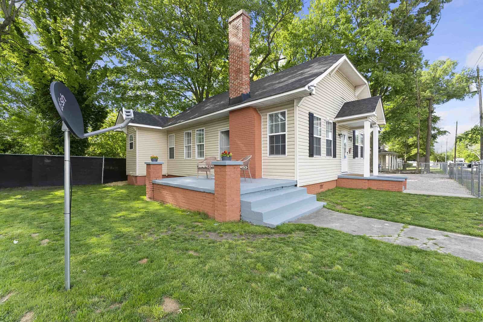 A single-story house with a mix of brick and siding, featuring a chimney, front porch, and a satellite dish on a well-manicured lawn.