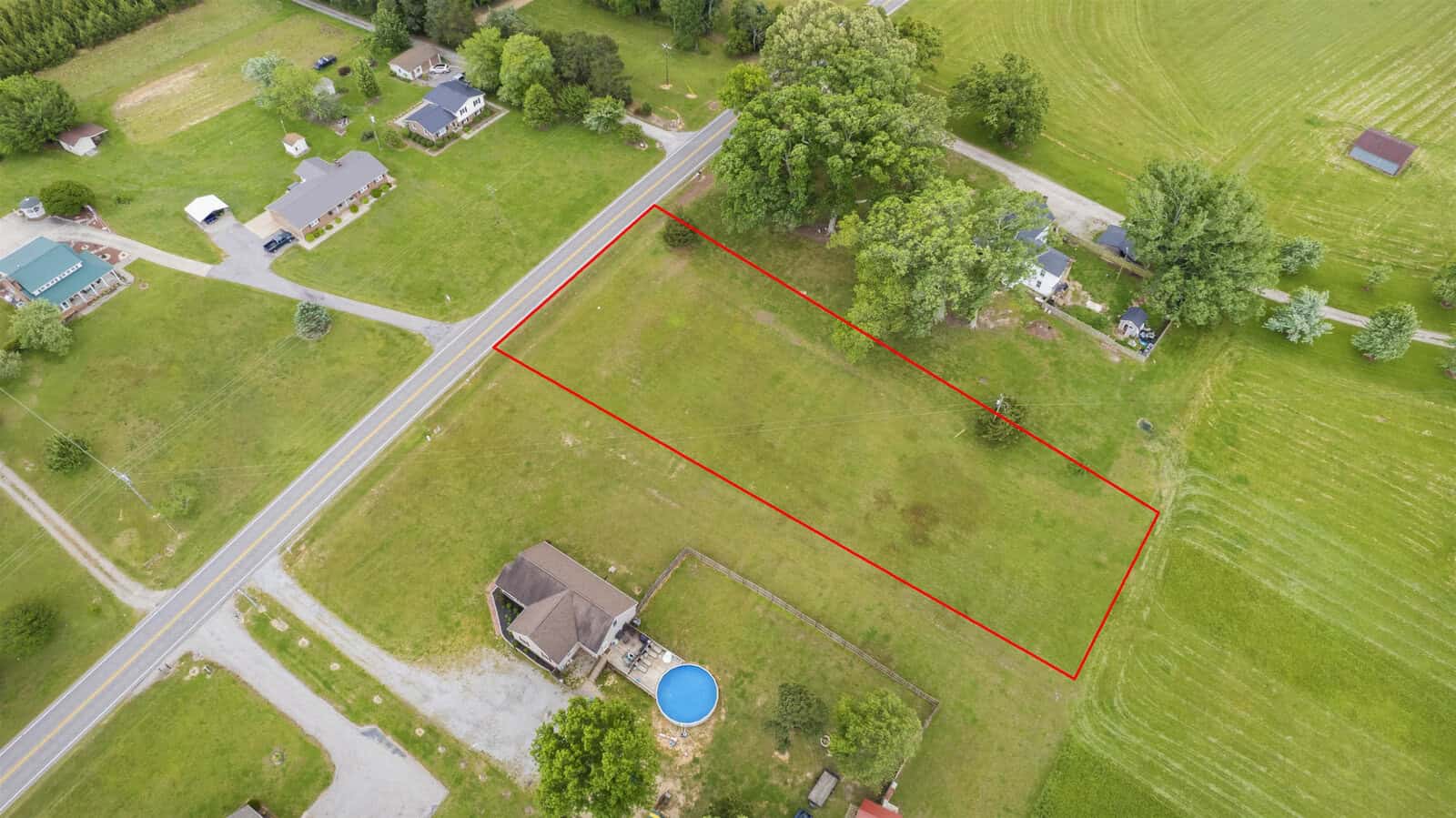Aerial view of a rectangular plot of land marked by a red boundary line, adjacent to a road with nearby residential properties.