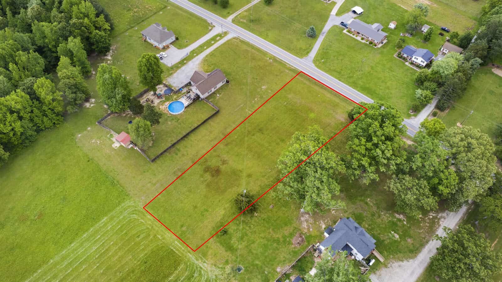 Aerial view of a property outlined in red, with surrounding houses and a green landscape.