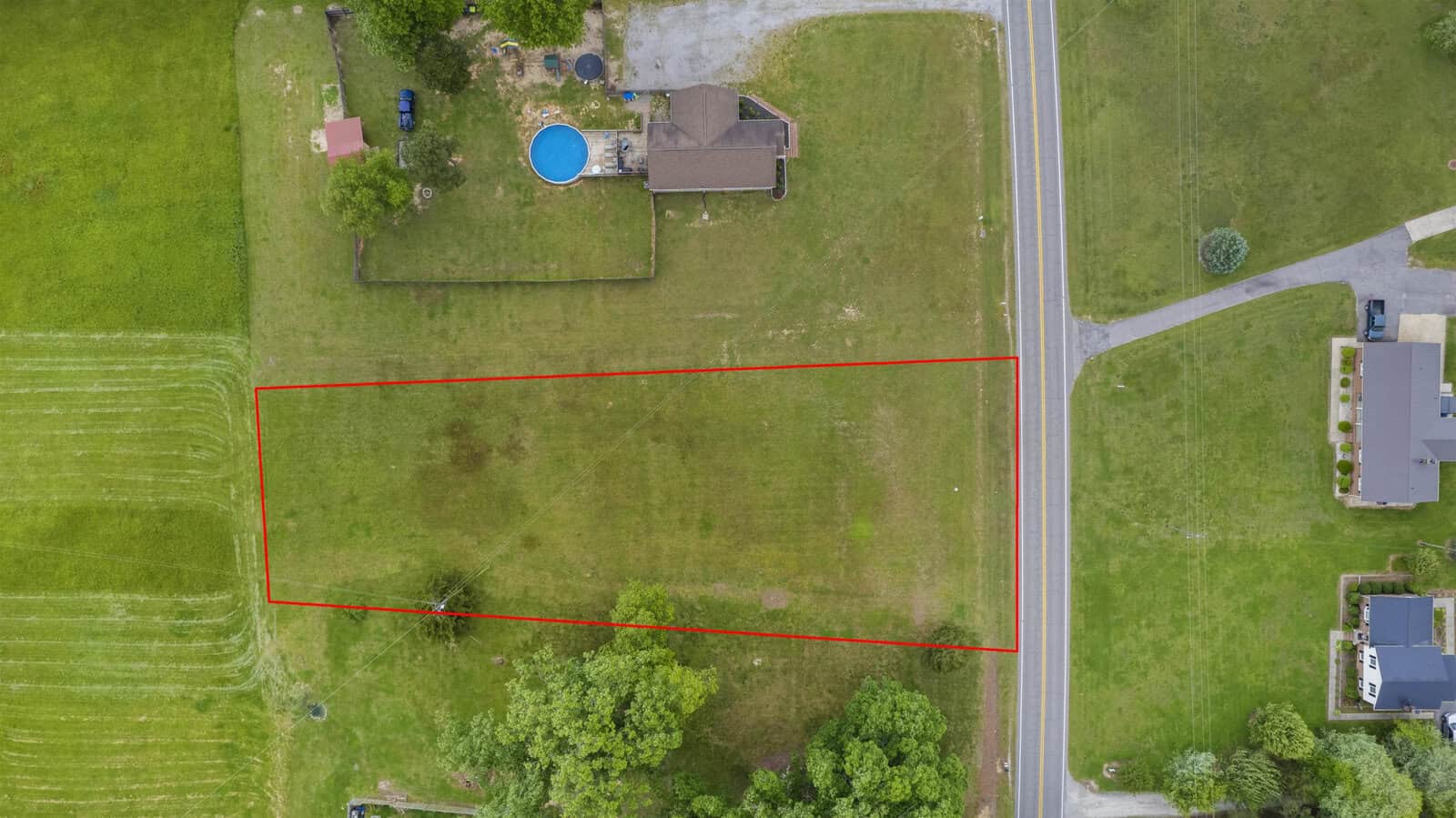 An aerial view of a vacant lot delineated by red lines adjacent to a residential property with a blue swimming pool.