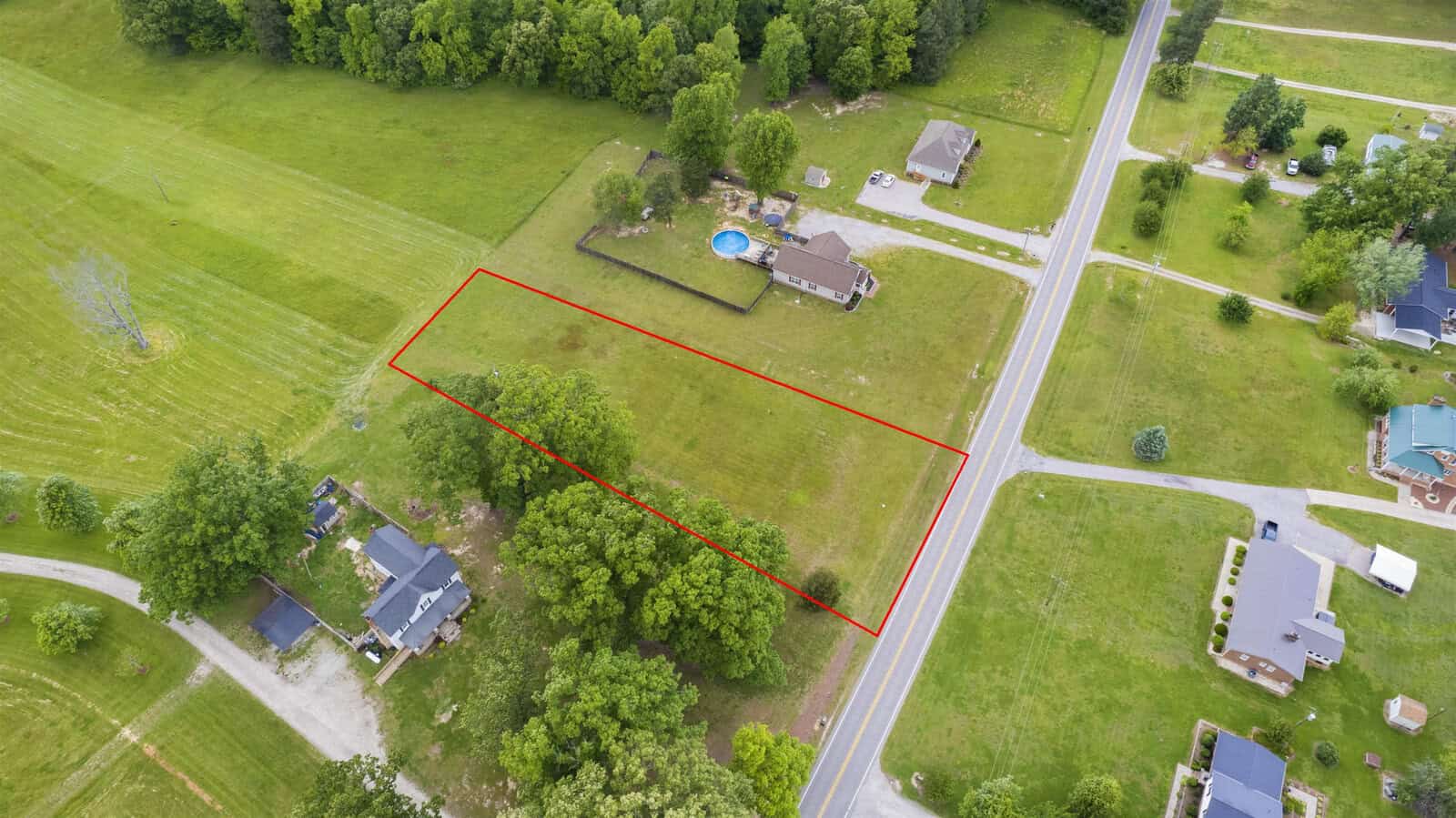 Aerial view of a suburban area with properties marked by a red outline, featuring a large grassy plot of land and surrounding homes.