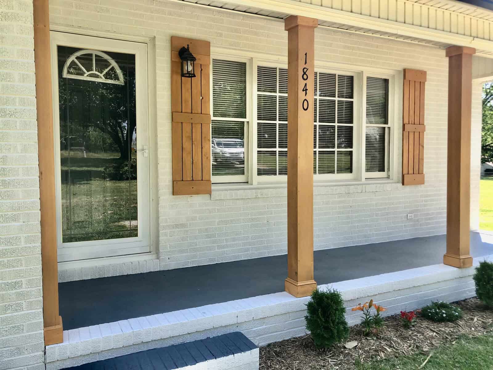 Front porch of a house with a cream exterior, featuring a white door, two windows with shutters, a porch light fixture, and the address number 1840 displayed prominently.