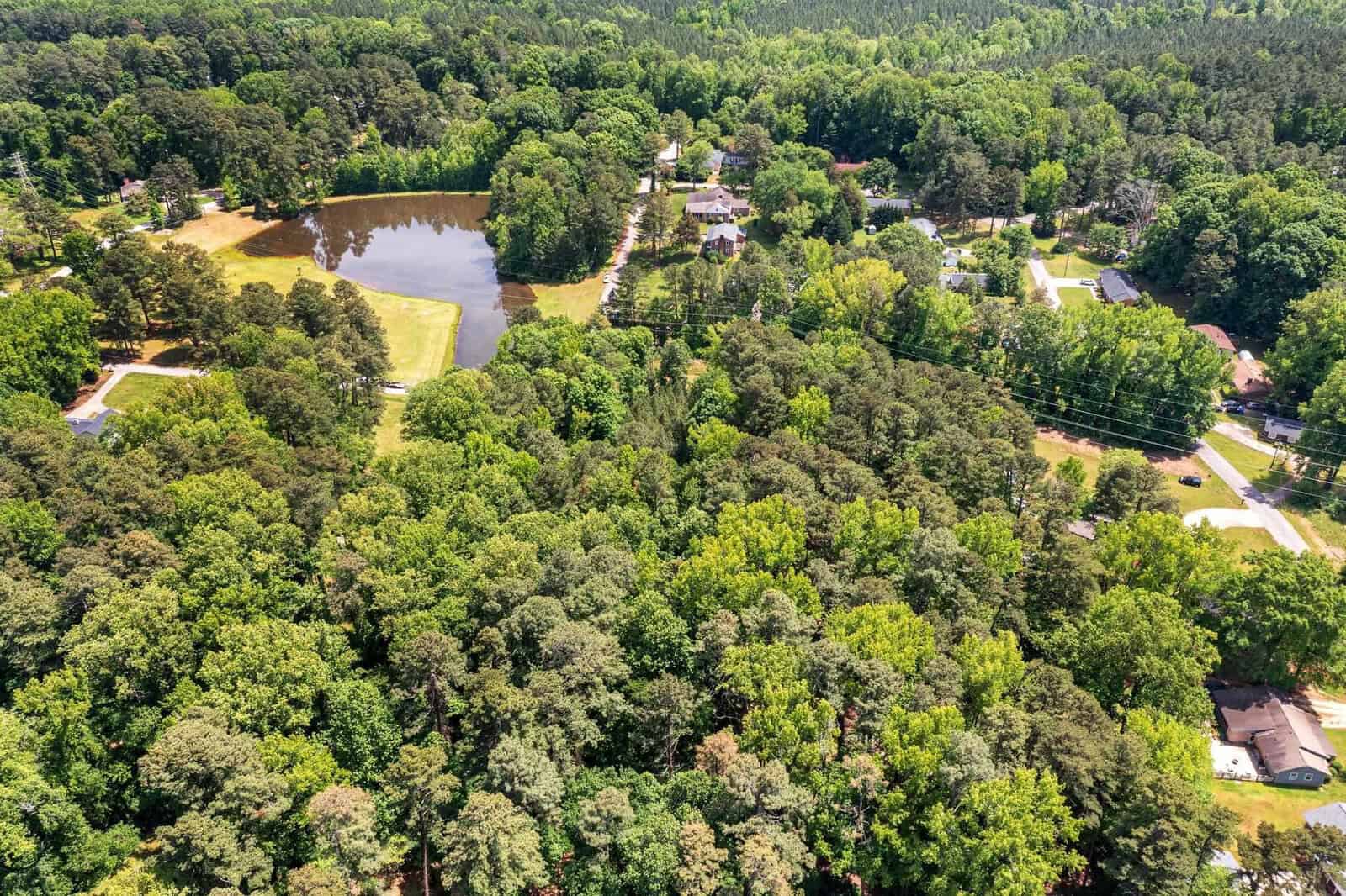 Aerial view of a residential area with houses surrounded by dense green trees and a small lake.