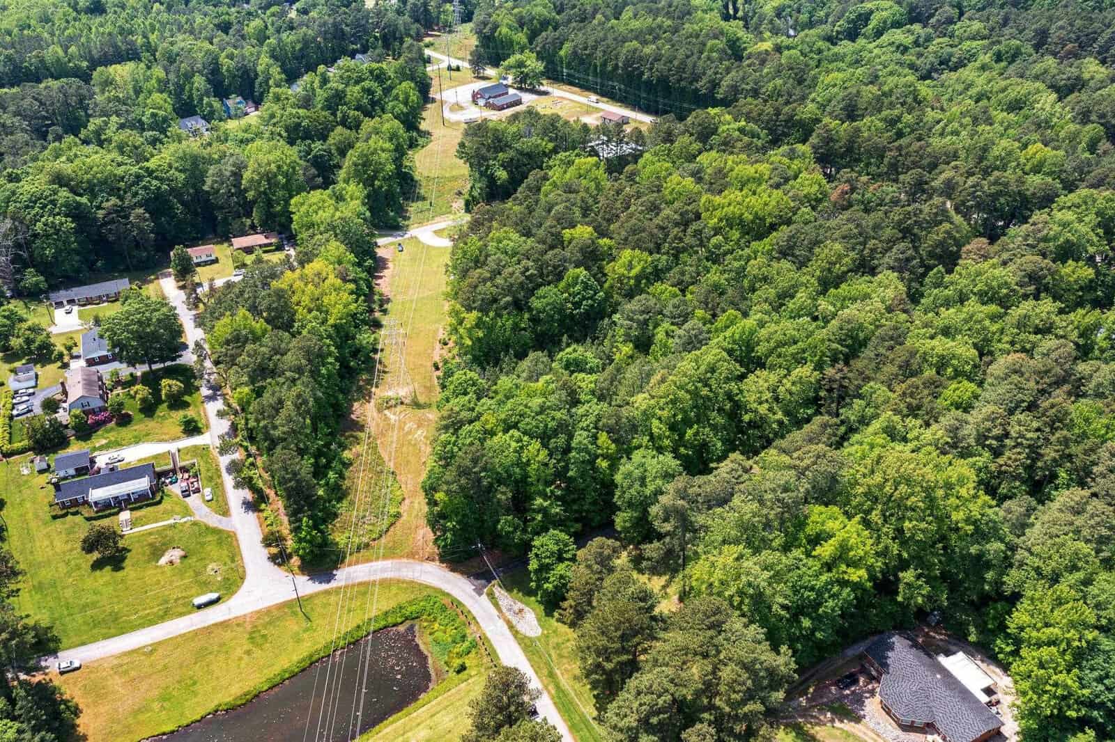 Aerial view of a suburban area showing a winding road, houses, and a large expanse of green trees with a clear-cut path through the forest.