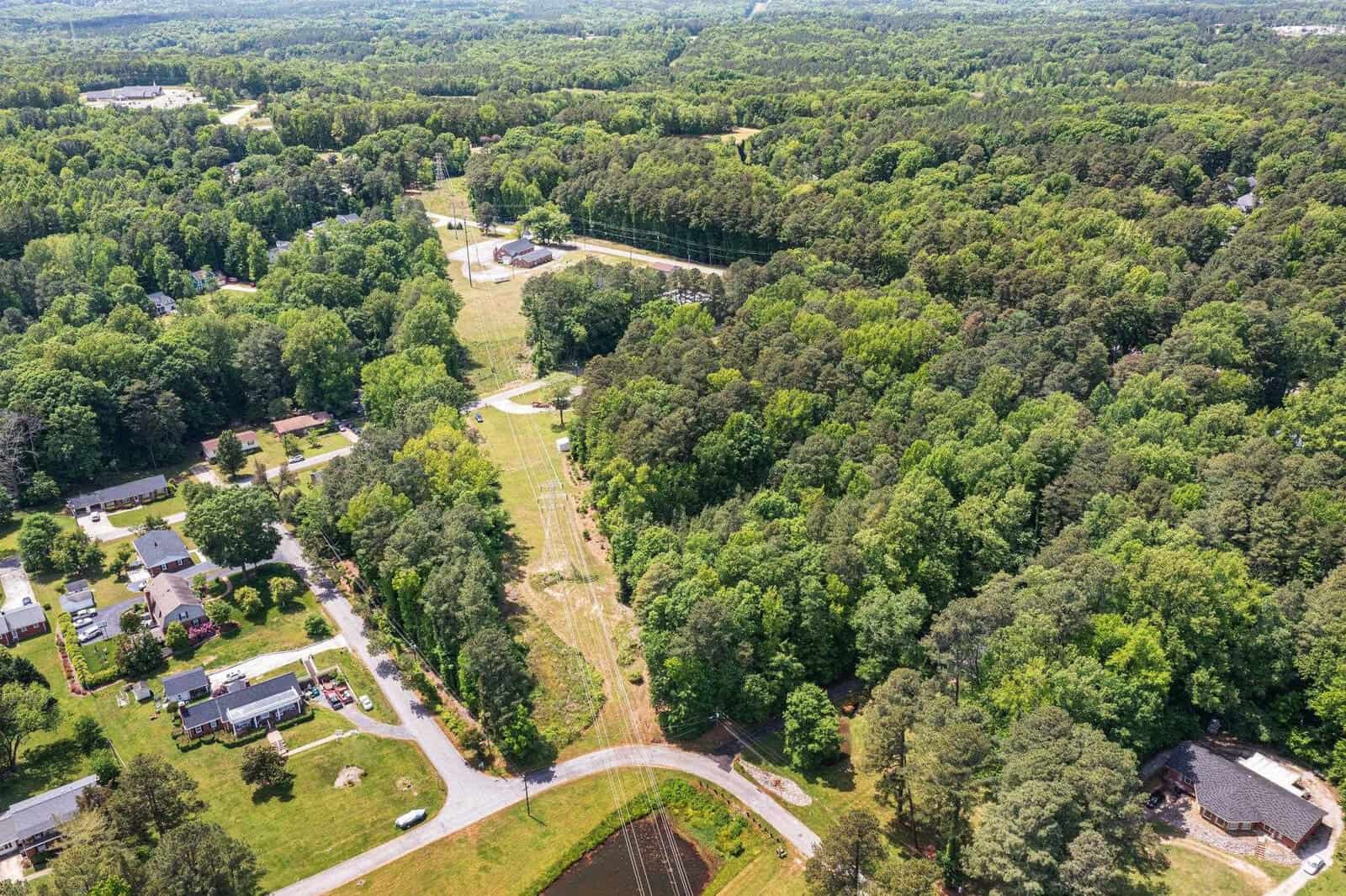 Aerial view of a suburban area with a straight path cutting through a densely wooded area, connecting a residential neighborhood to other infrastructure.