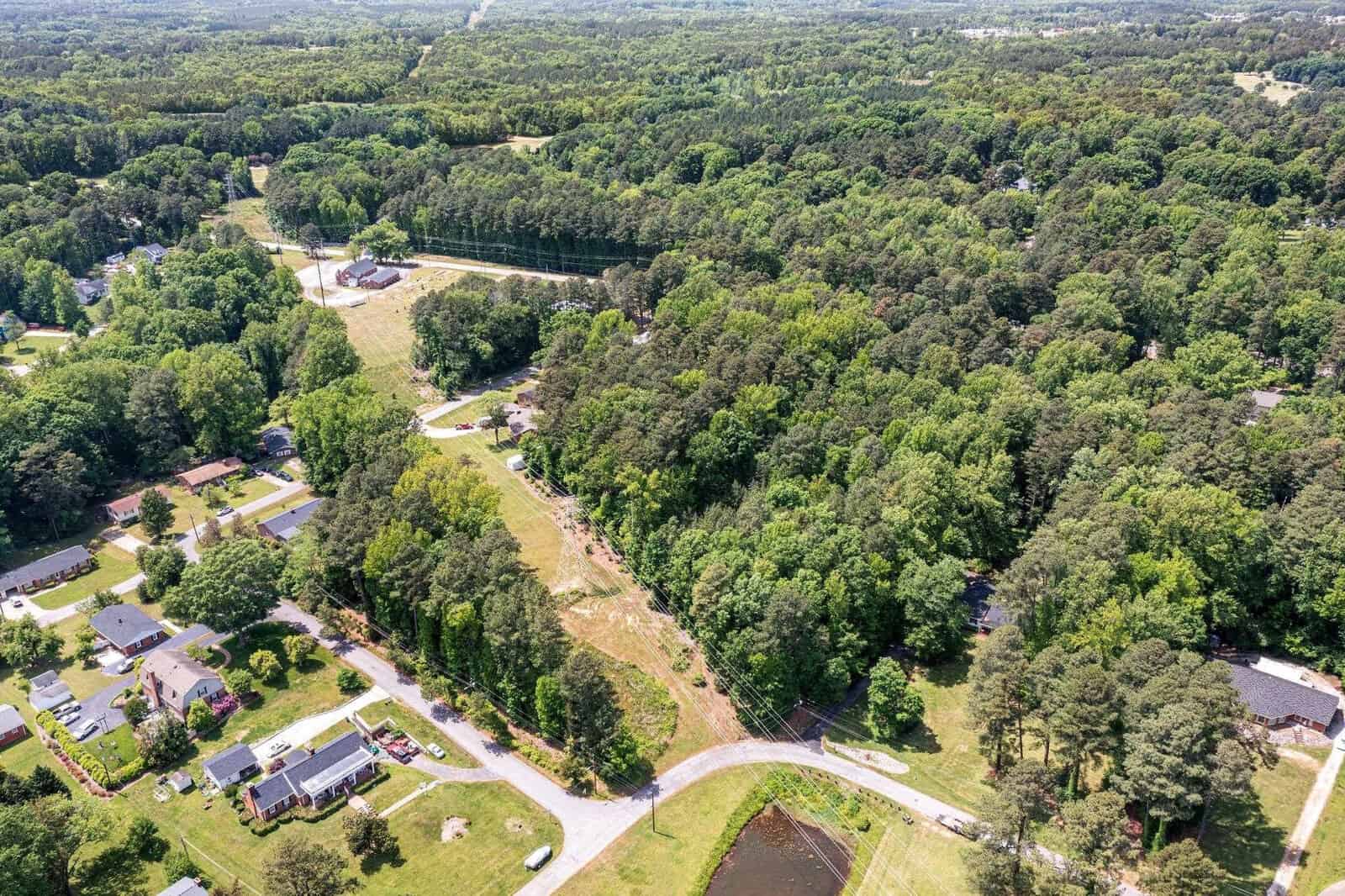 Aerial view of a suburban area with houses surrounded by dense greenery and a clear road cutting through the landscape.