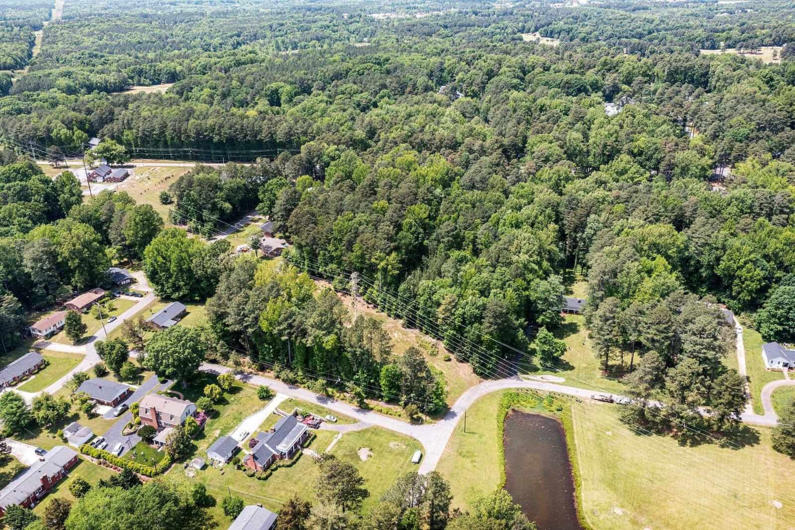 Aerial view of a residential area with houses surrounded by lush green trees and a winding road running through the neighborhood.