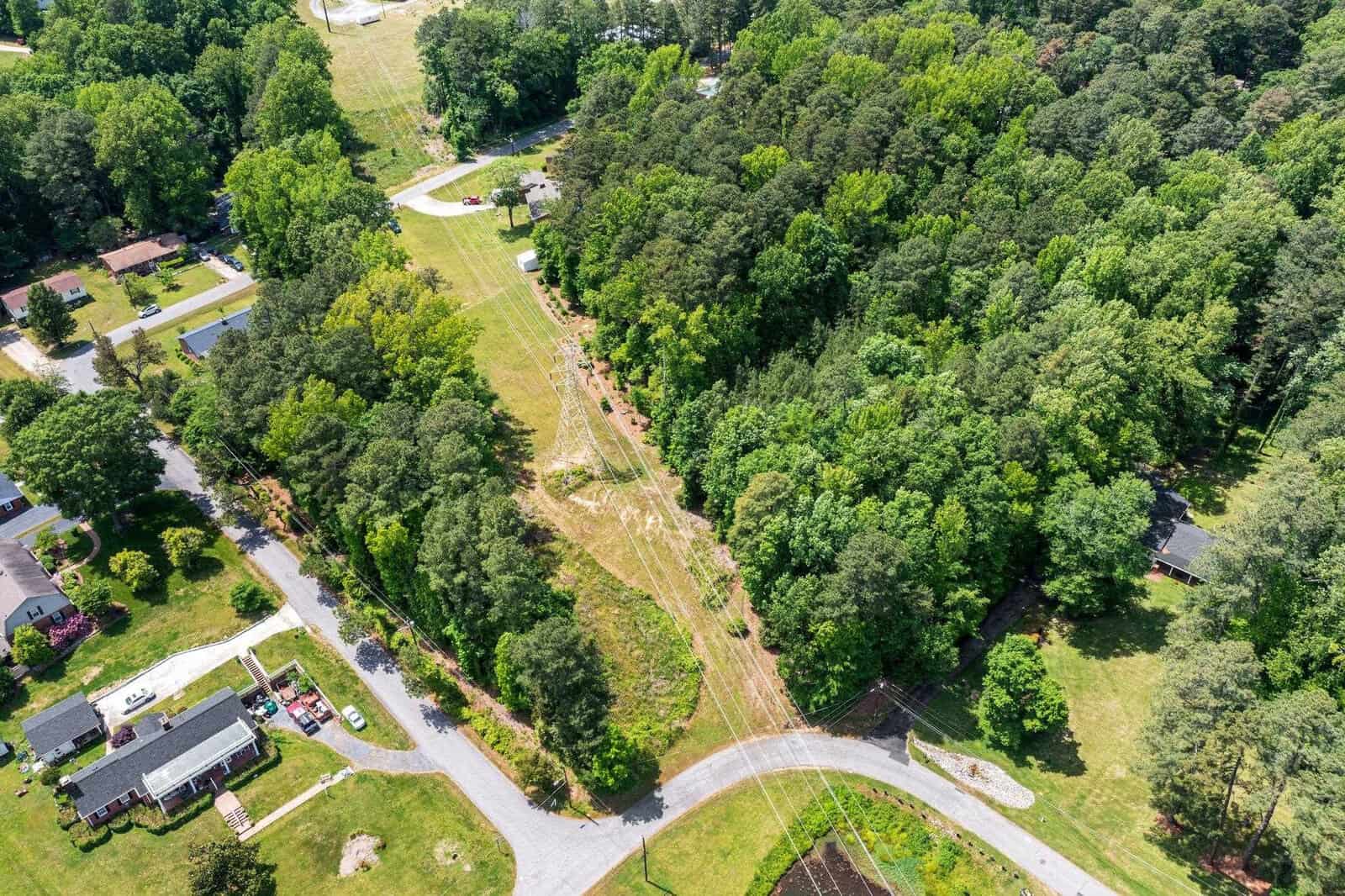 Aerial view of a suburban area with a clear path cutting through trees and houses on either side.