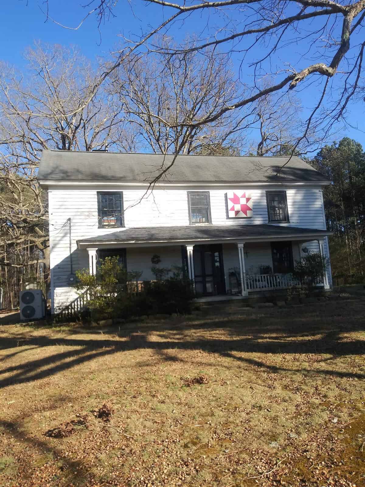 A two-story white house with a front porch, adorned with a star decoration, located at 315 S Lynnbank Road, Henderson NC, surrounded by a lawn with trees under a clear blue sky.