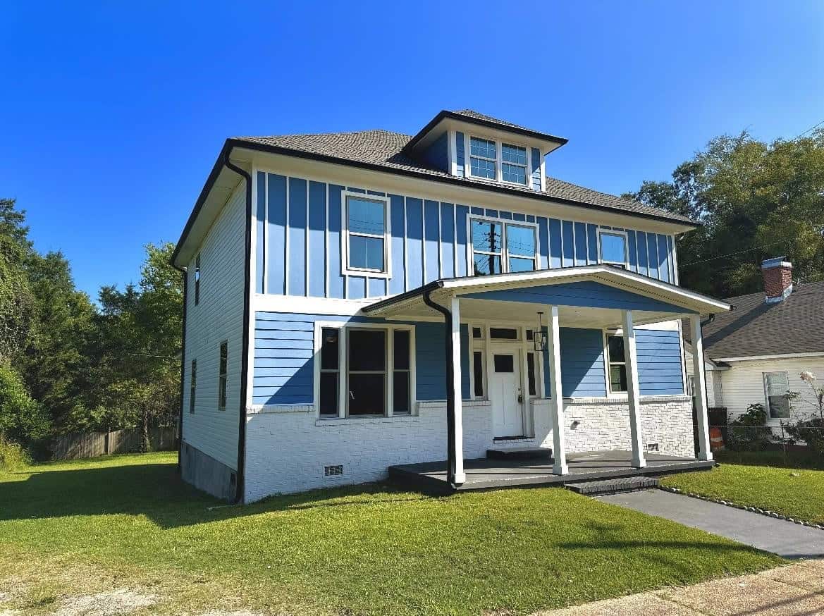 A two-story blue and white house with a covered front porch and a clear blue sky in the background.